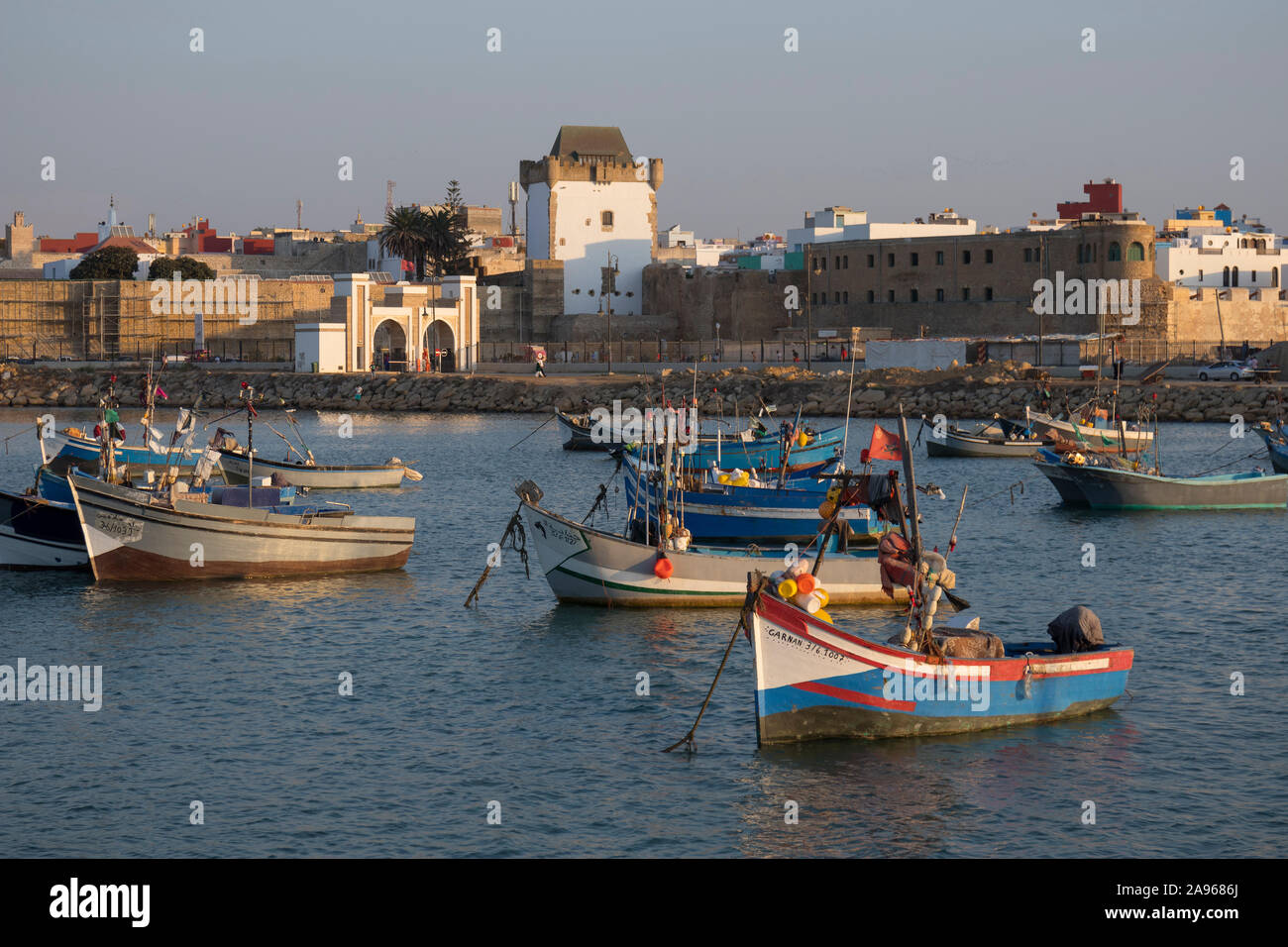Asilah, Morocco-September 10, 2019: Traditional blue fishing boats in the harbour of Asilah with Al-Kamra tower in the medina on the background , Moro Stock Photo
