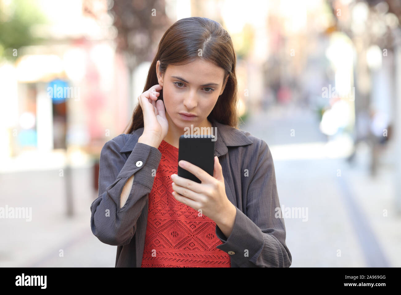 Front view of a serious girl using mobile phone touching hair walking in the street Stock Photo