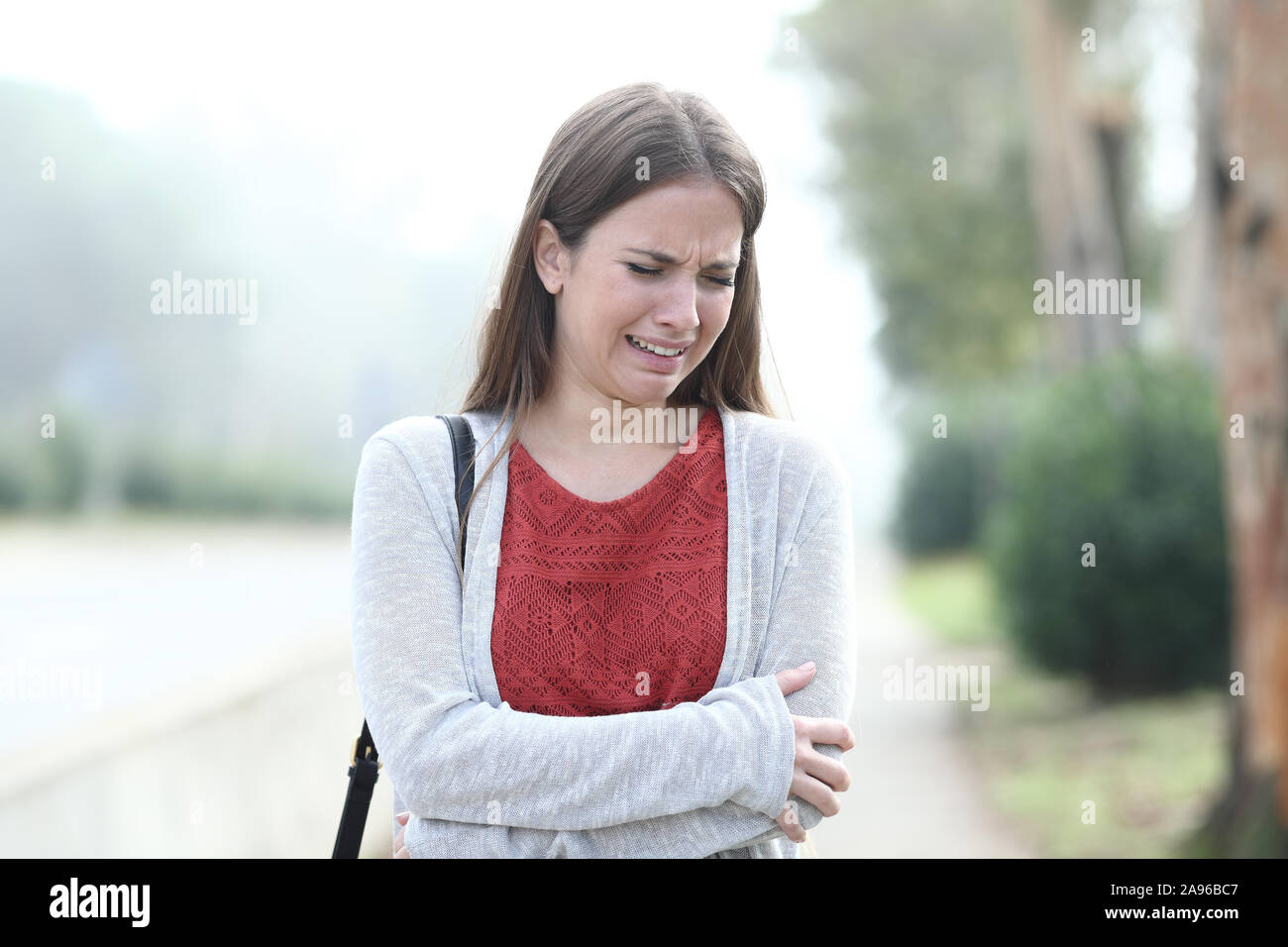 Front view portrait of a sad woman crying alone walking in a foggy park Stock Photo