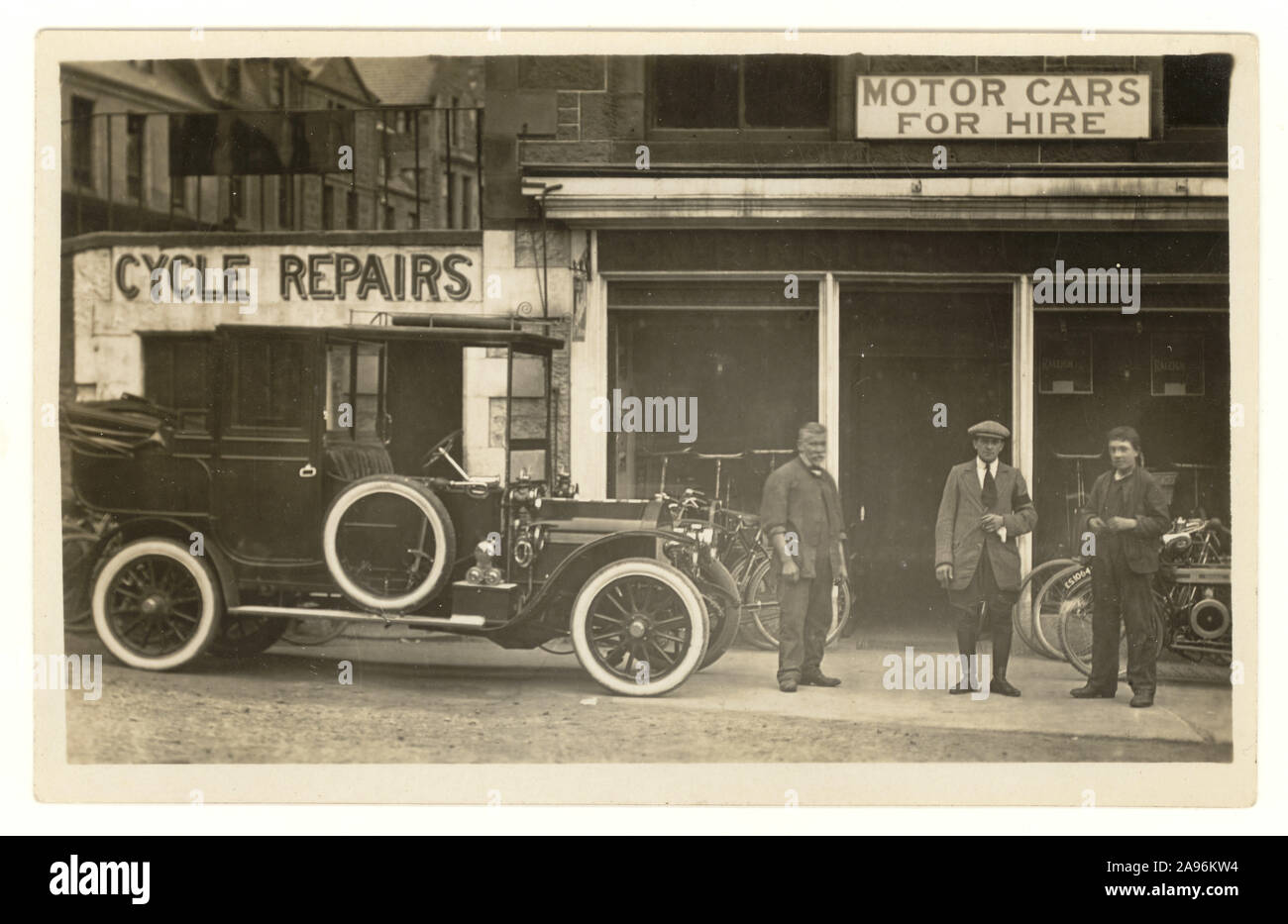Original early 1900's postcard of cycle repair shop and motor car hire shop, with vintage car outside, circa 1920's, Dundee, Scotland, registration on bike. Stock Photo