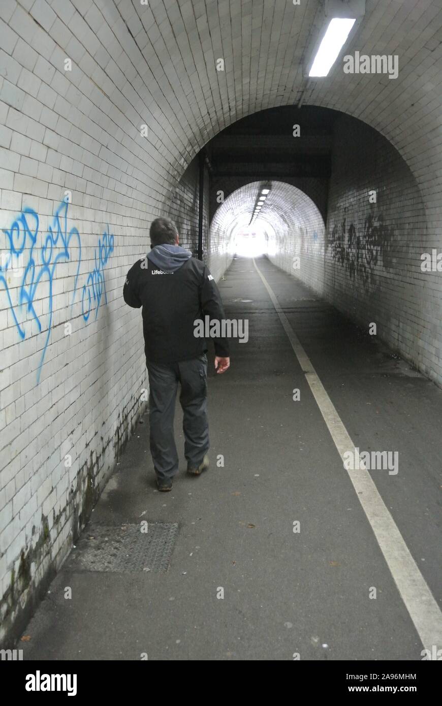 Unidentifiable man using mobile phone whilst walking along underneath the railway bridge in