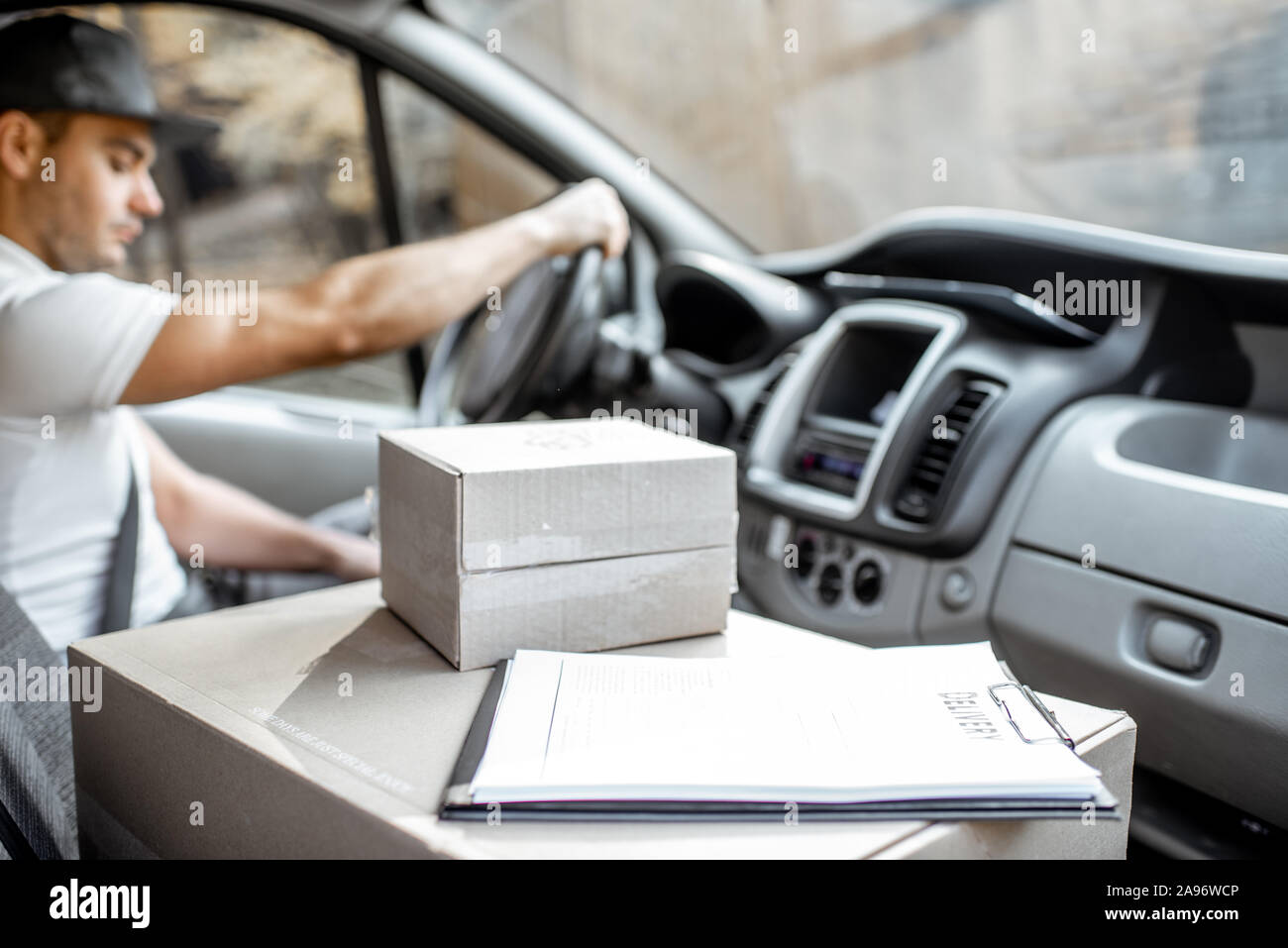 Delivery man driving cargo vehicle with parcels on the passenger seat