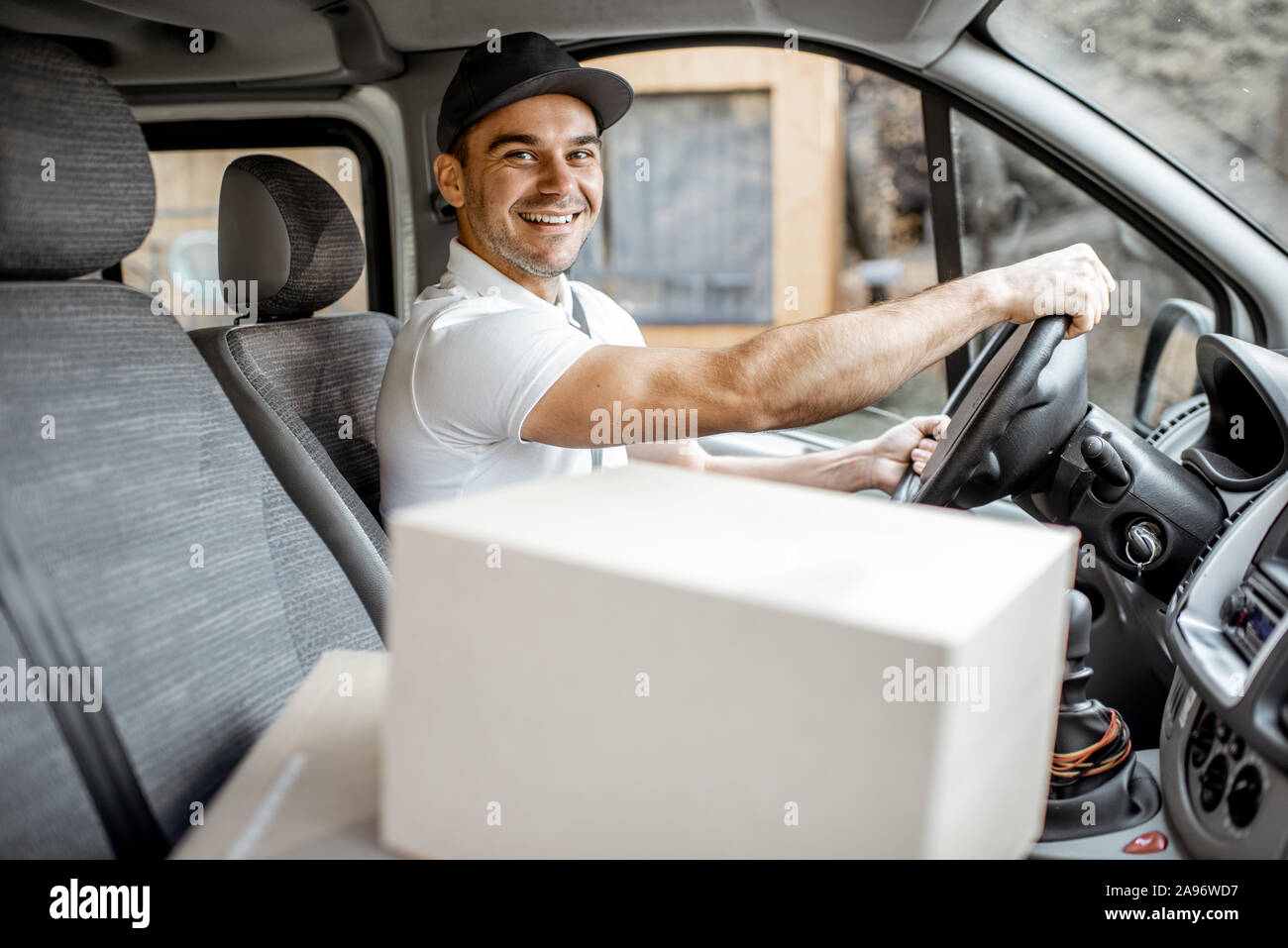 Delivery man driving cargo vehicle with parcels on the passenger seat