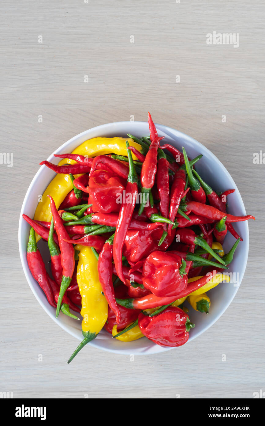 Bowl of fresh mixed chili peppers, red, orange and yellow hot peppers on a wooden table viewed from above, habanero, lemon drop, thai peppers Stock Photo