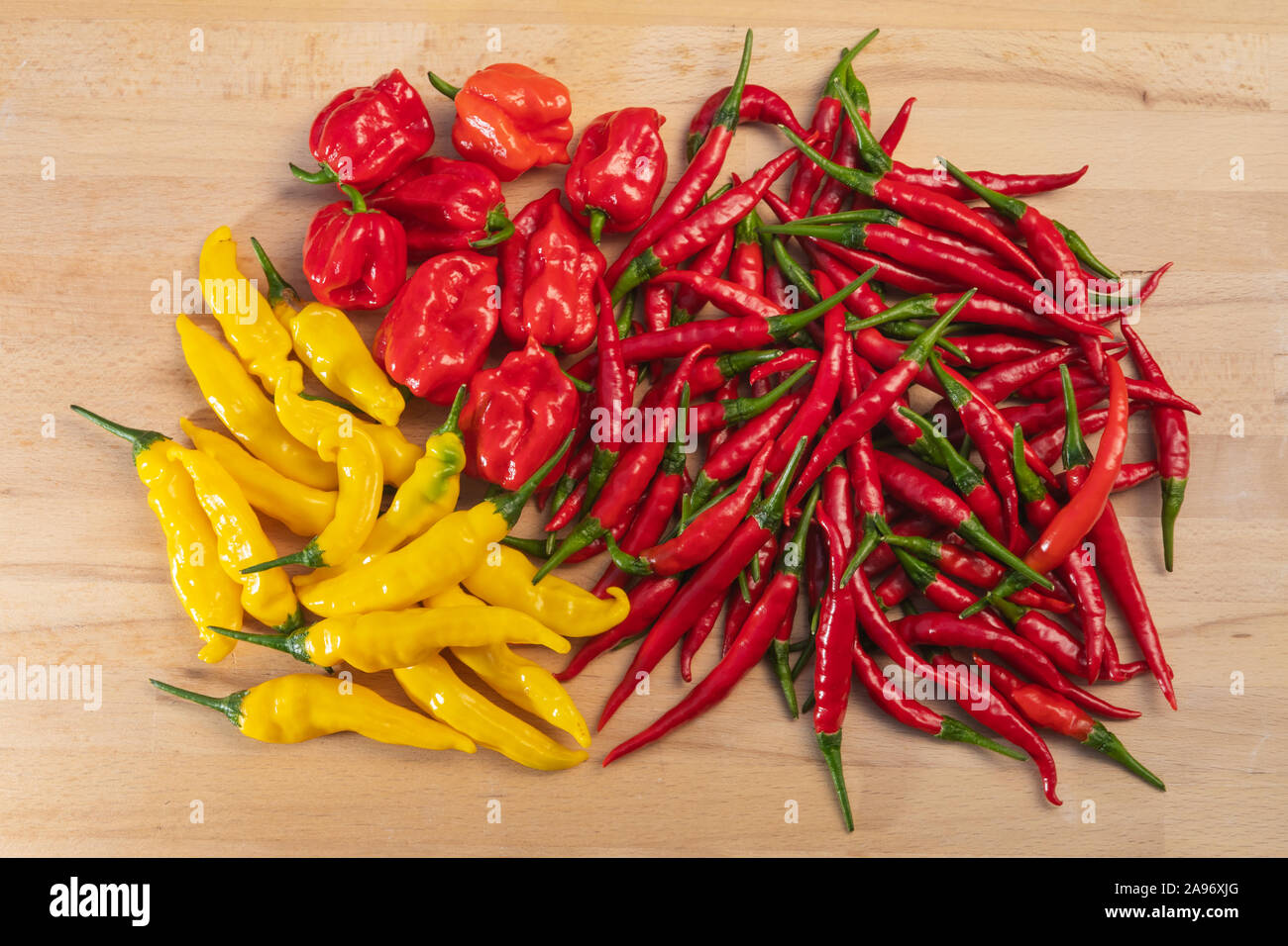 Fresh assorted chili peppers, red, orange and yellow hot peppers on a wooden table viewed from above, habanero, lemon drop, thai chilli pepper Stock Photo