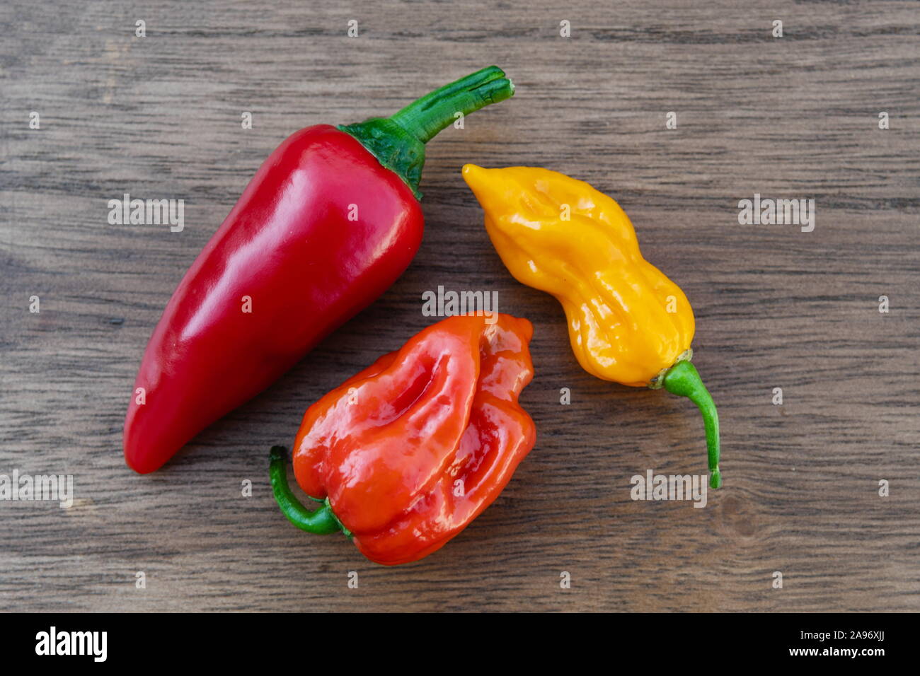 Three fresh organic chili peppers, red, orange and yellow hot peppers on a wooden table viewed from above, habanero, fatali, cayenne Stock Photo