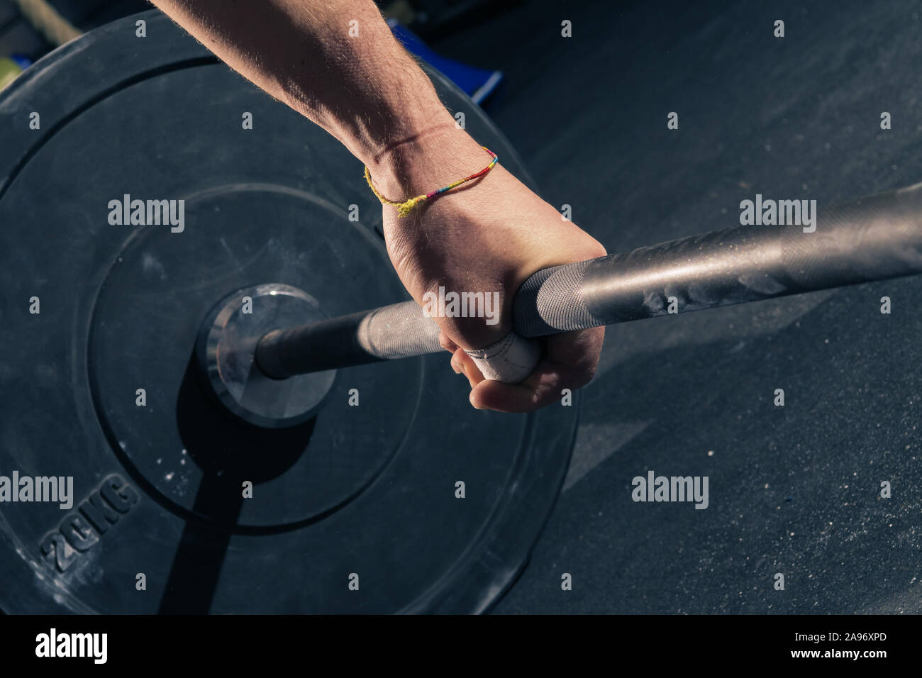 Closeup of man's left hand with bracelet hook gripping a barbell with 20kg plates Stock Photo