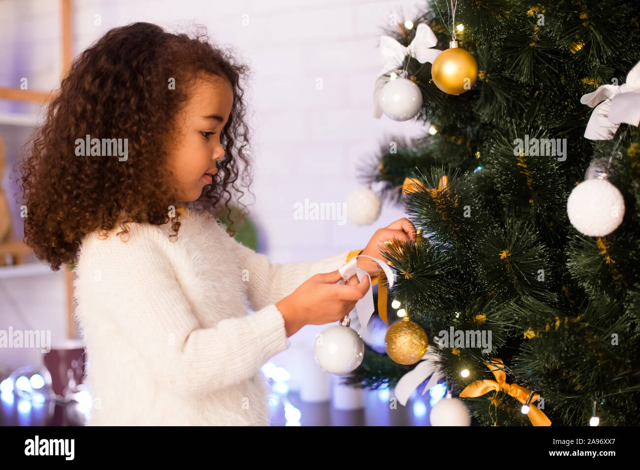 Christmas tradition. Little afro girl decorating Xmas tree at home ...