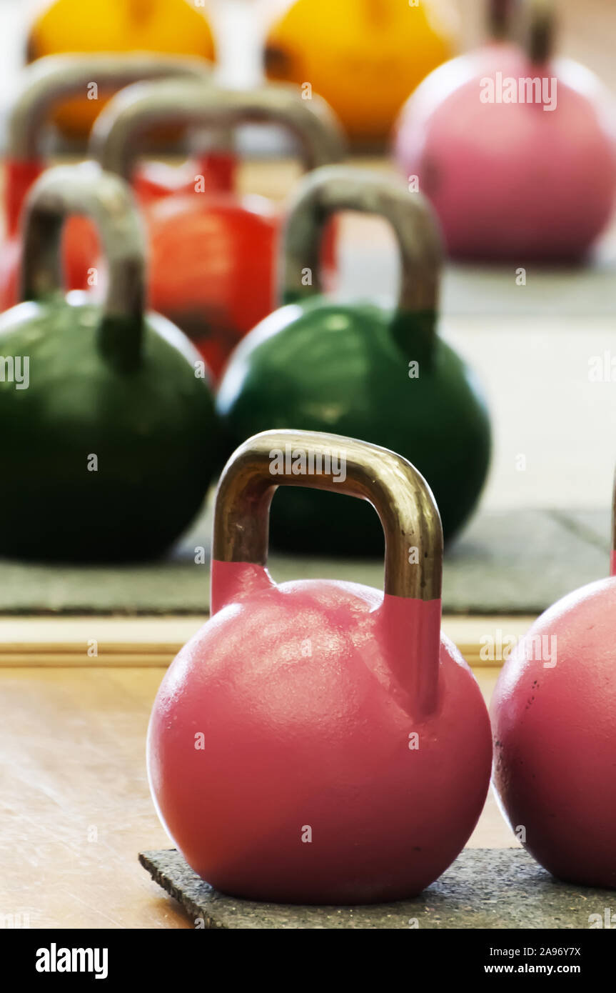 Kettlebells or cast-steel balls with handle of various colors and weights on gym floor. Sports, functional training and equipment. Stock Photo