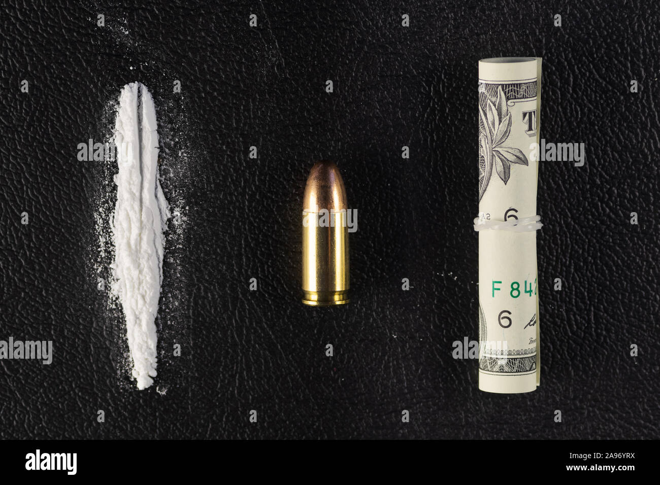 A line of cocaine powder, a single 9 mm bullet and dollar bill scroll. Conceptual mockup of illegal drug dealing, trafficking, war on drugs. Stock Photo