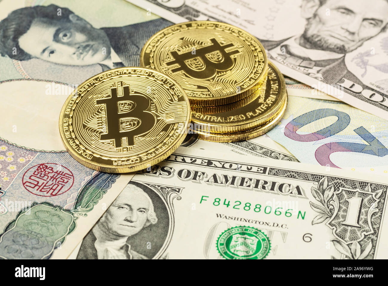Closeup of four Bitcoin cryptocurrency coins laid on top of US Dollar, Japanese Yen and Euro banknotes Stock Photo