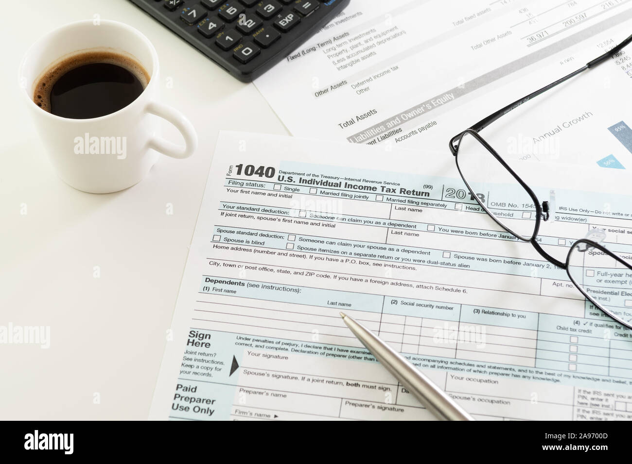White tabletop with U.S. income tax return form 1040, visible cup of coffee, pen, calculator and eyeglasses. Tax, accounting, business and finance Stock Photo