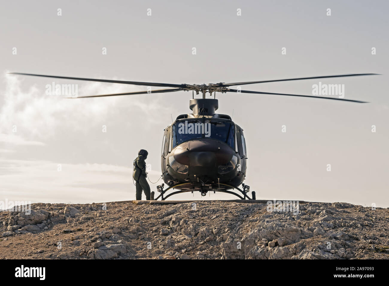 Pilot checking military helicopter before taking off from helipad on top of mountain. Military, airforce, defense and mountain rescue concepts. Stock Photo