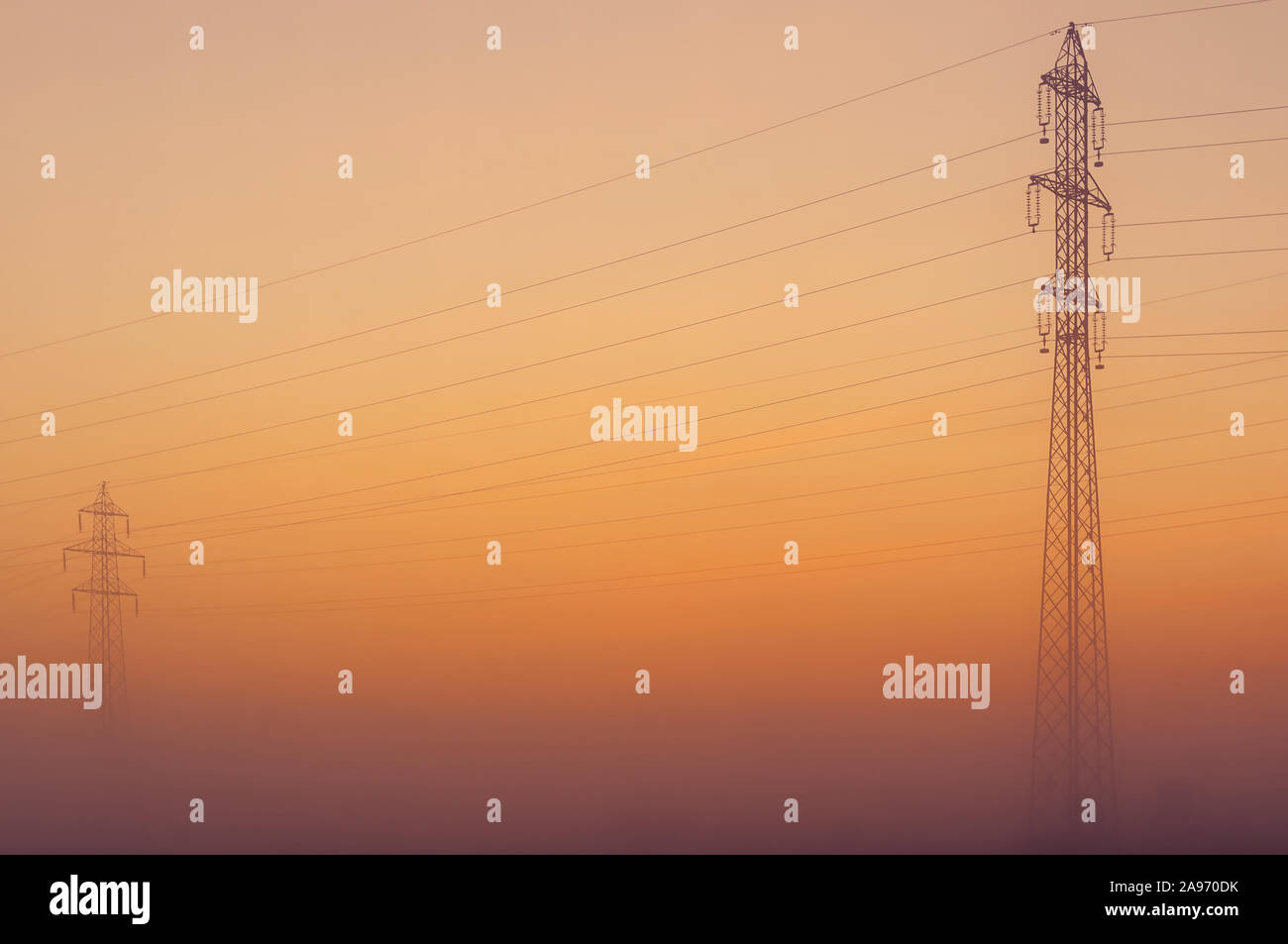 Transmission towers emerging from fog with orange twilight sky in background. Electricity, power transmission and distribution, electrical energy Stock Photo