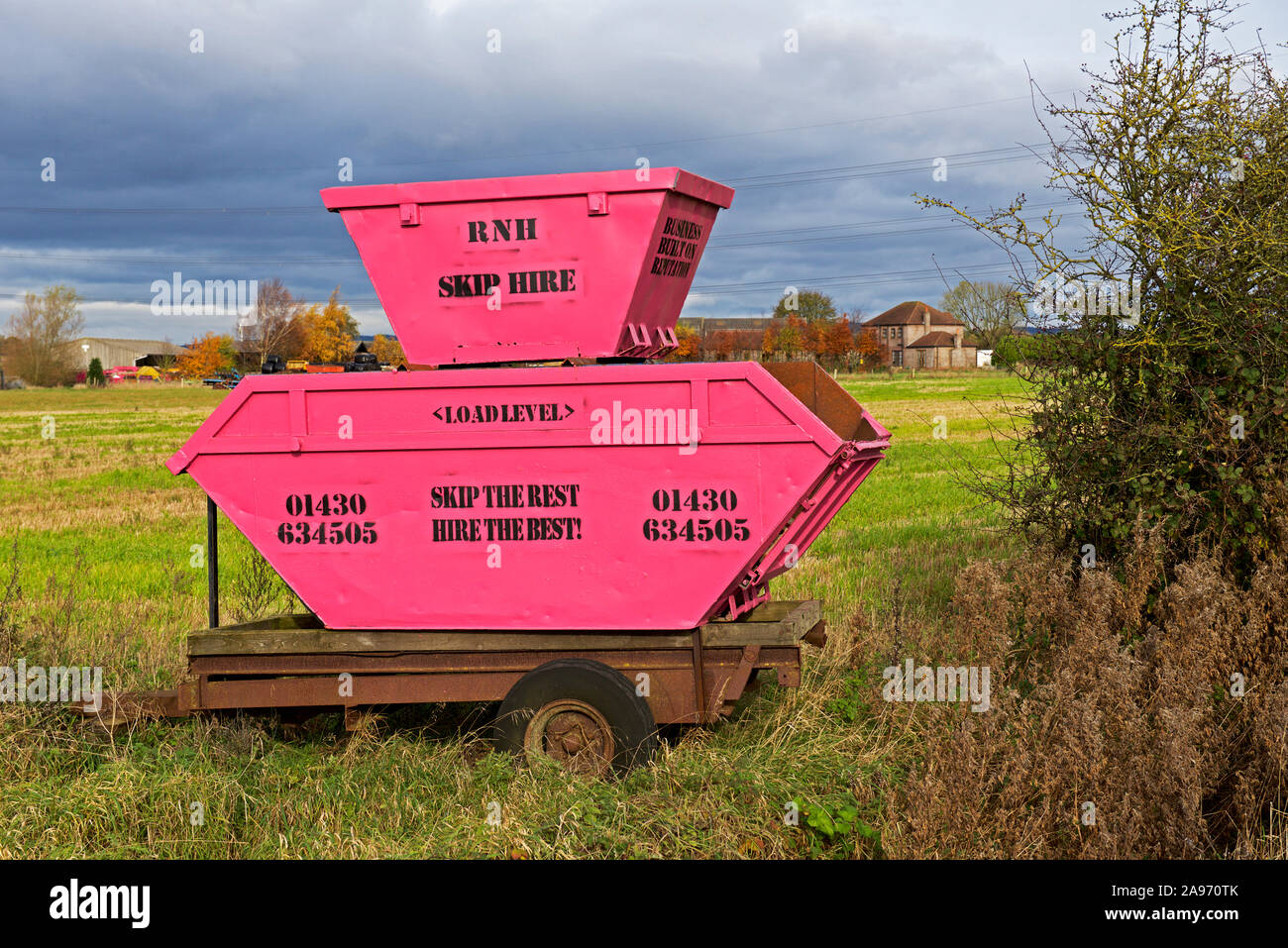 Pink rubbish skips on display in the corner of a field, to advertise a
