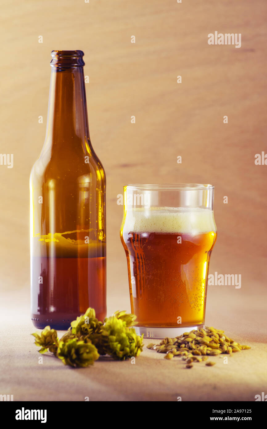 Bottle and glass of beer with barley and hops on wooden background. Craft beer, brewery and alcohol beverage concepts. Stock Photo