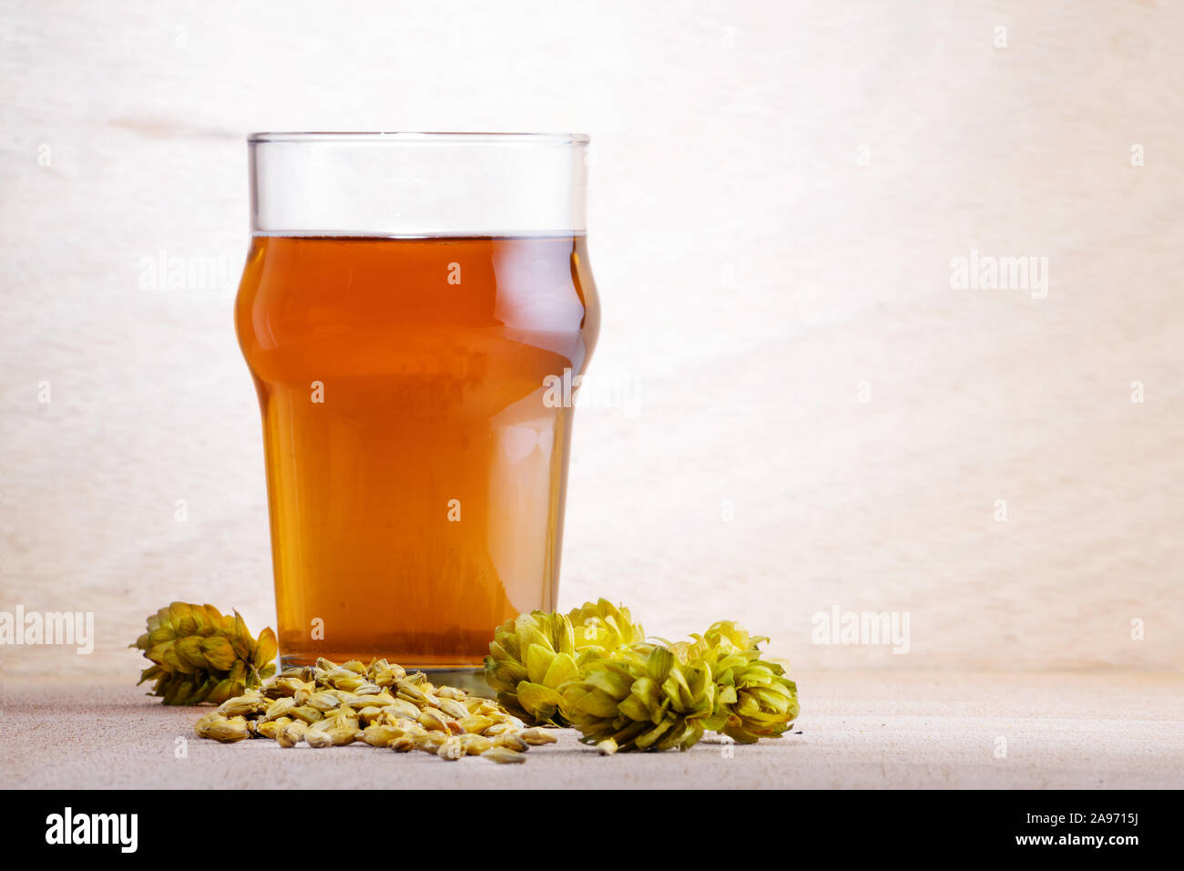 Beer in a glass with barley and hops on light wooden background. Craft beer, brewery and alcohol beverage concepts. Stock Photo