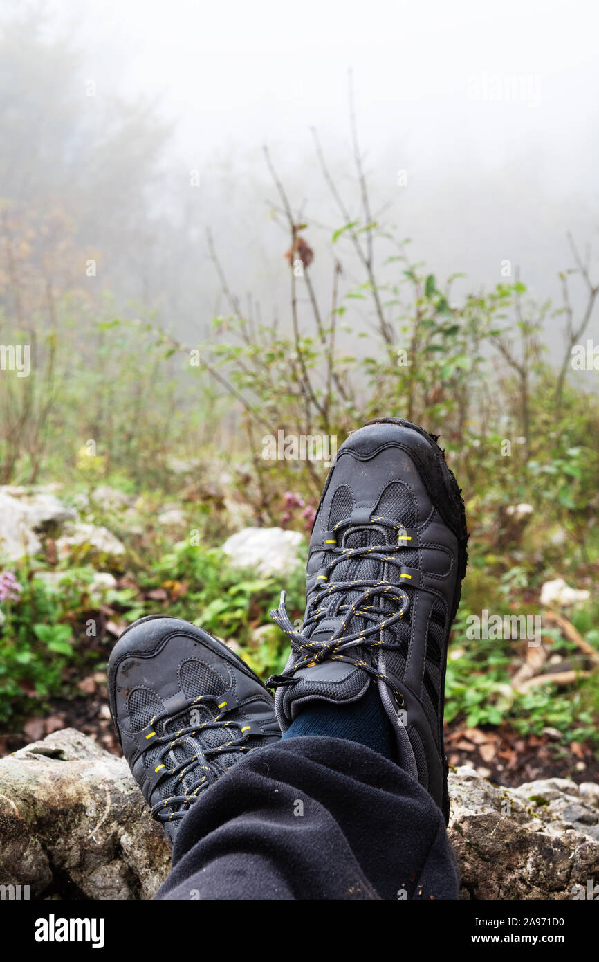 Crossed hiker's feet with gray trekking shoes and foggy forest in background. Hiking, backpacking and equipment concepts. Stock Photo