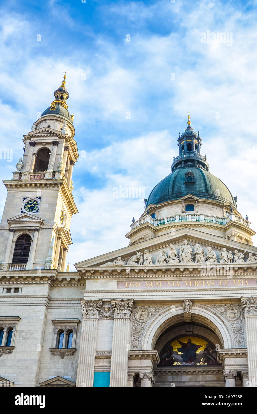 Vertical picture of the front side facade of Saint Stephen's Basilica in Budapest, Hungary with blue sky and clouds above. Roman Catholic basilica built in neoclassical style. Left tower and cupola. Stock Photo