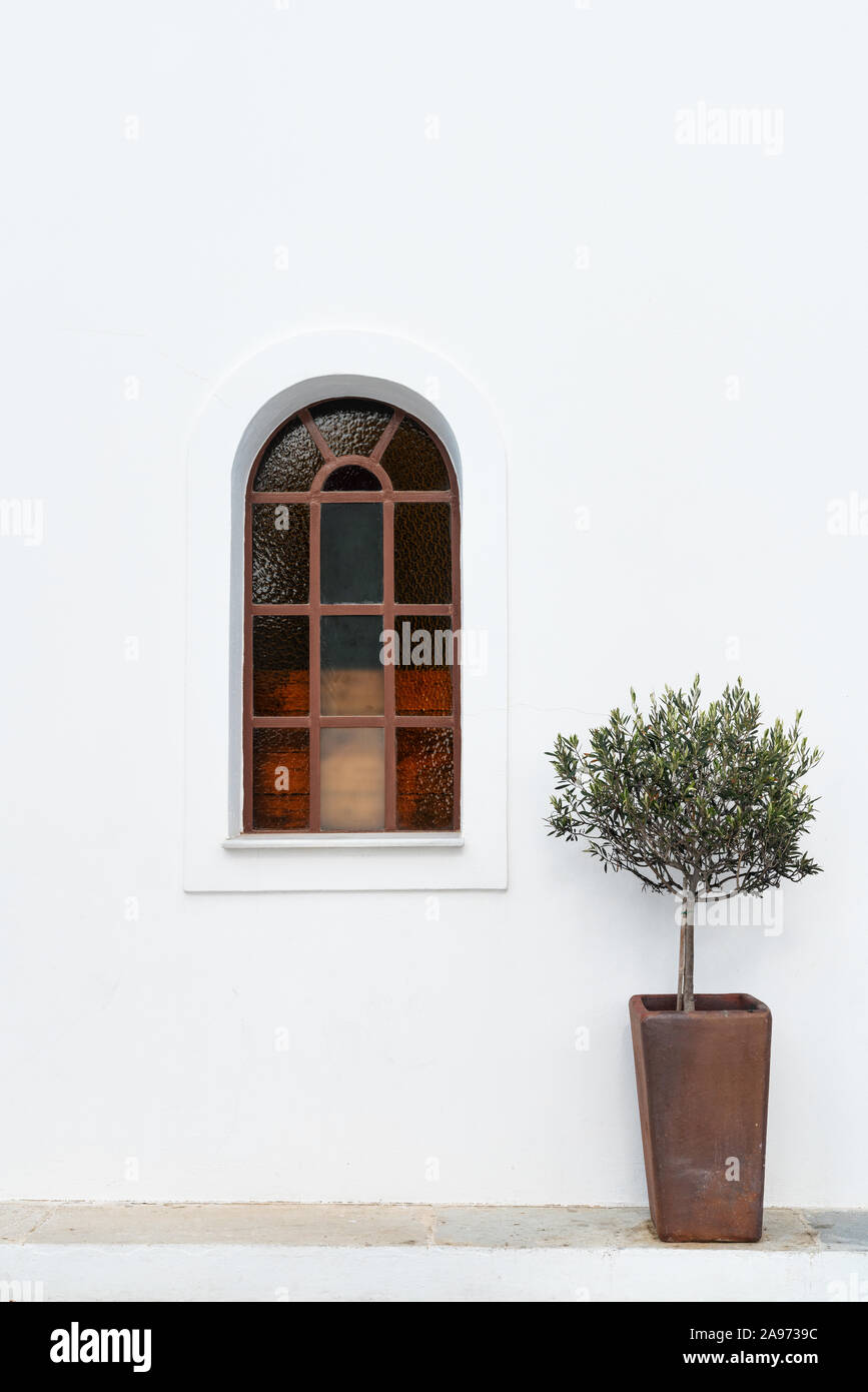 Arched top plain stained glass window on a whitewashed building. Stock Photo