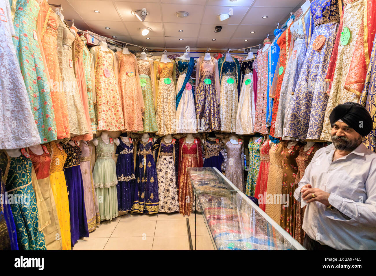 Shop manager with Punjabi, Indian and Asian dresses and saris on display, traditional, colourful evening wear and clothes, Southall, London, UK Stock Photo