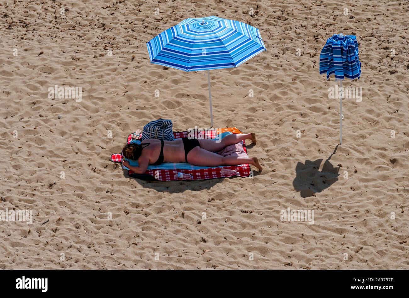 Middle-aged woman lying in the shadow of a parasol on the beach of the Mediterranean harbour at the deep blue sea Stock Photo