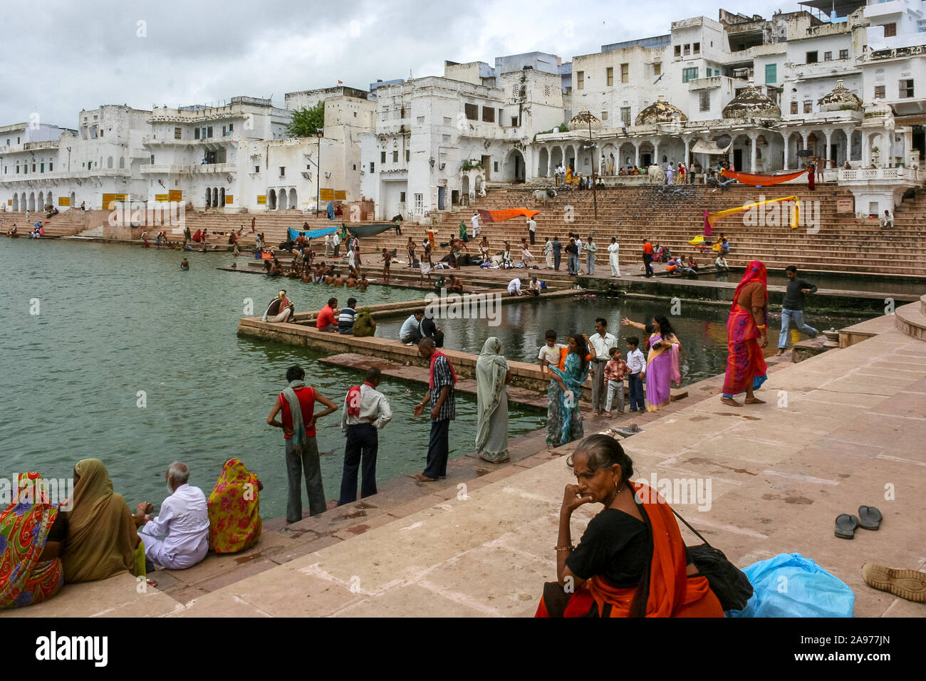 Pushkar, Rajasthan, India:  Indian people sit or walk  on the shores (ghat) of the holy Pushkar lake while some women blow wet saris in the wind. Stock Photo