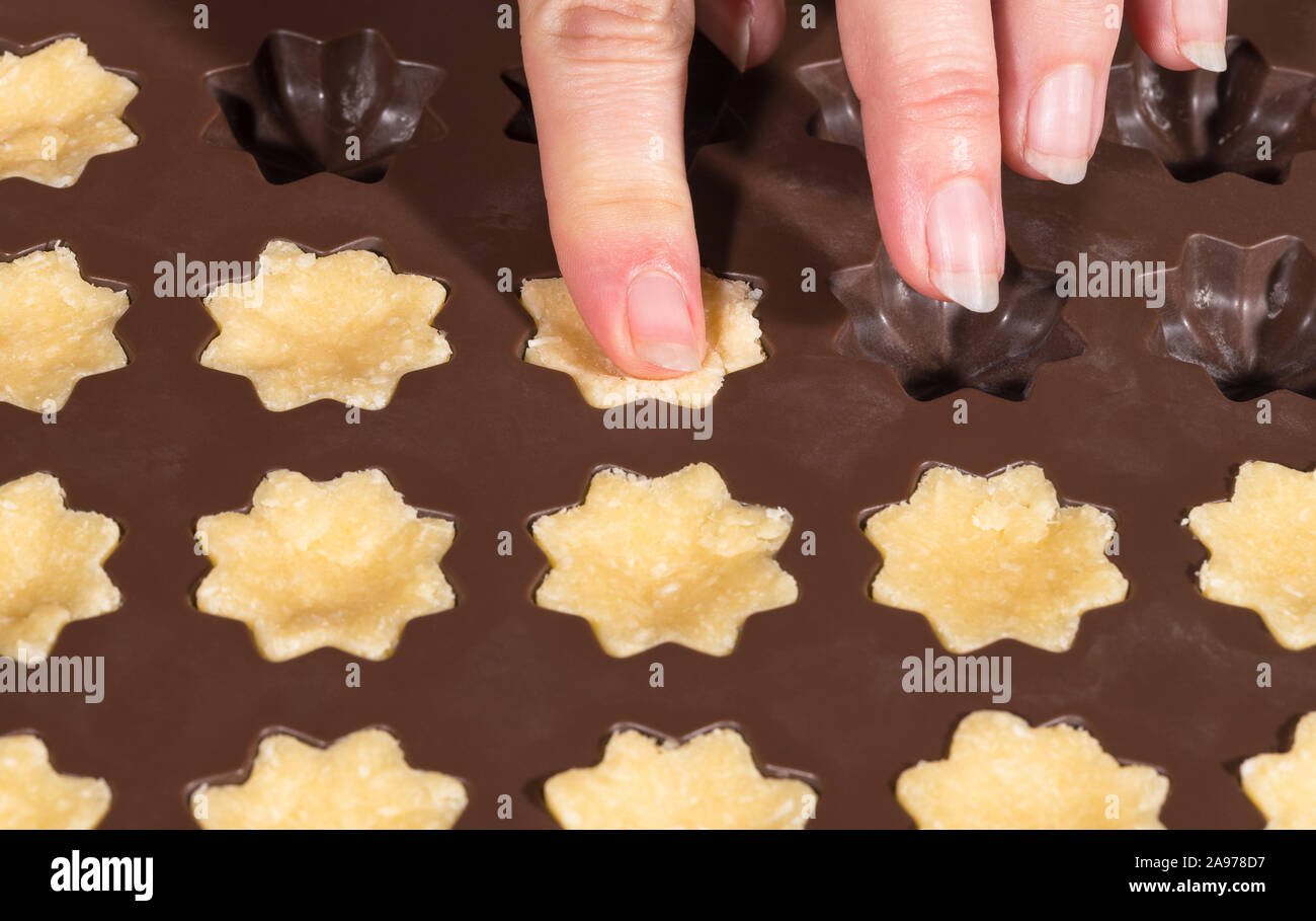 Female fingers filling brown silicone mold. Baking of Xmas coconut cupcakes. Ornate flowers full of sweet raw dough. Holiday cookies in plastic form. Stock Photo