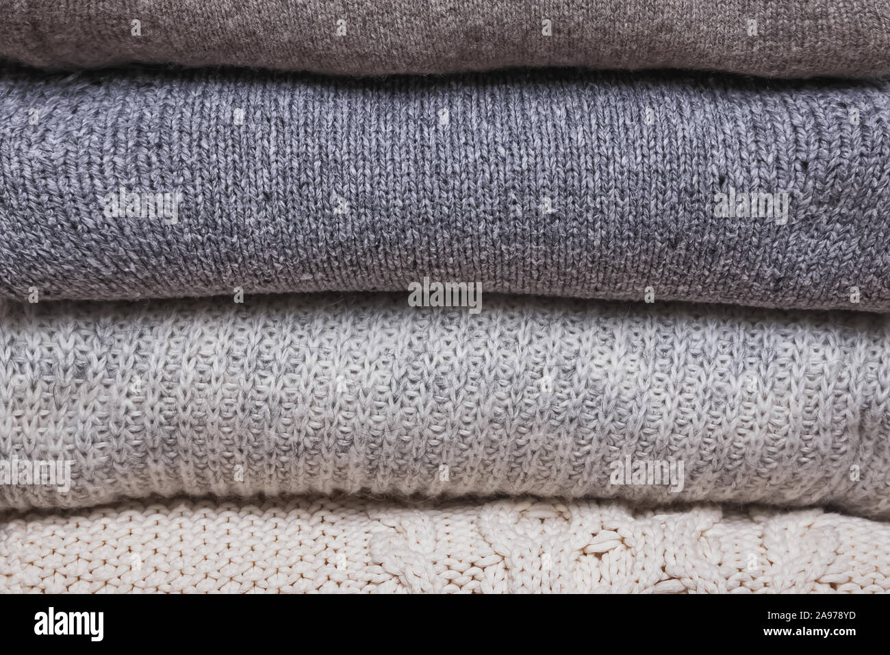 Bunch of knitted warm sweaters, different knitting patterns folded in stack Stock Photo