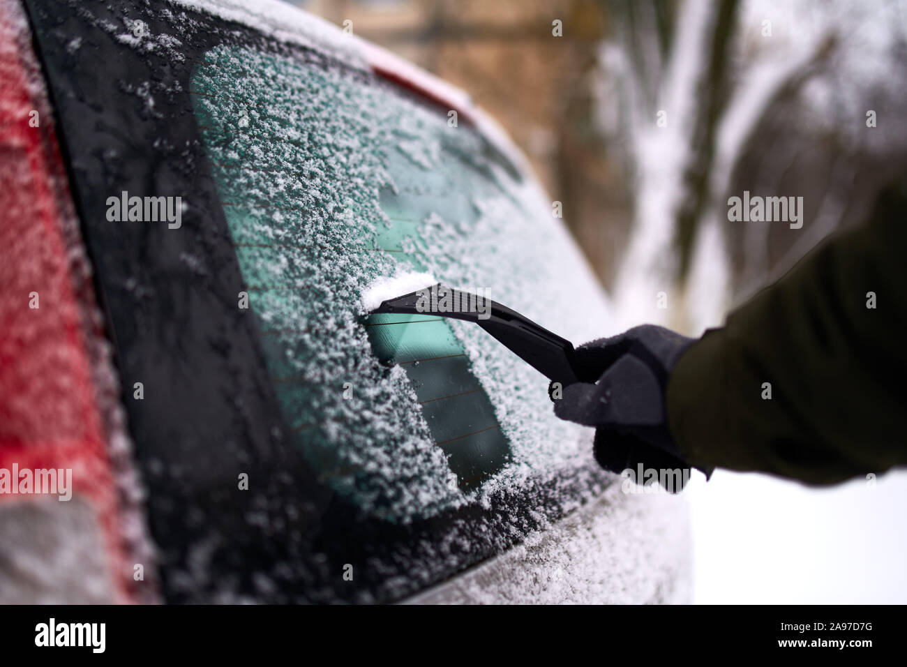 Cleaning the rear car window of snow with ice scraper before the trip
