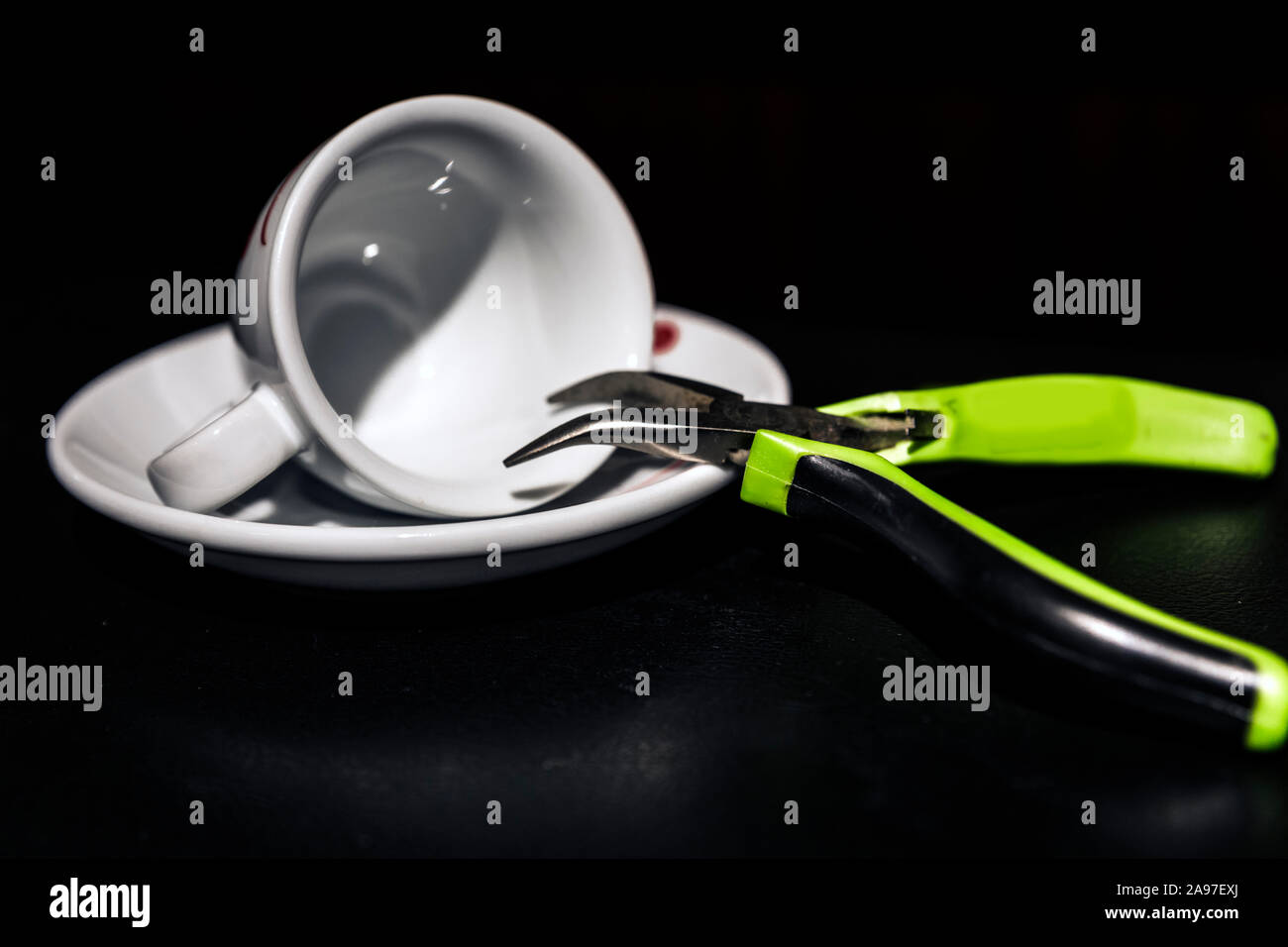 Interior shot of needle nose pliers sticking nose into an empty espresso cup on neutral black background. Stock Photo
