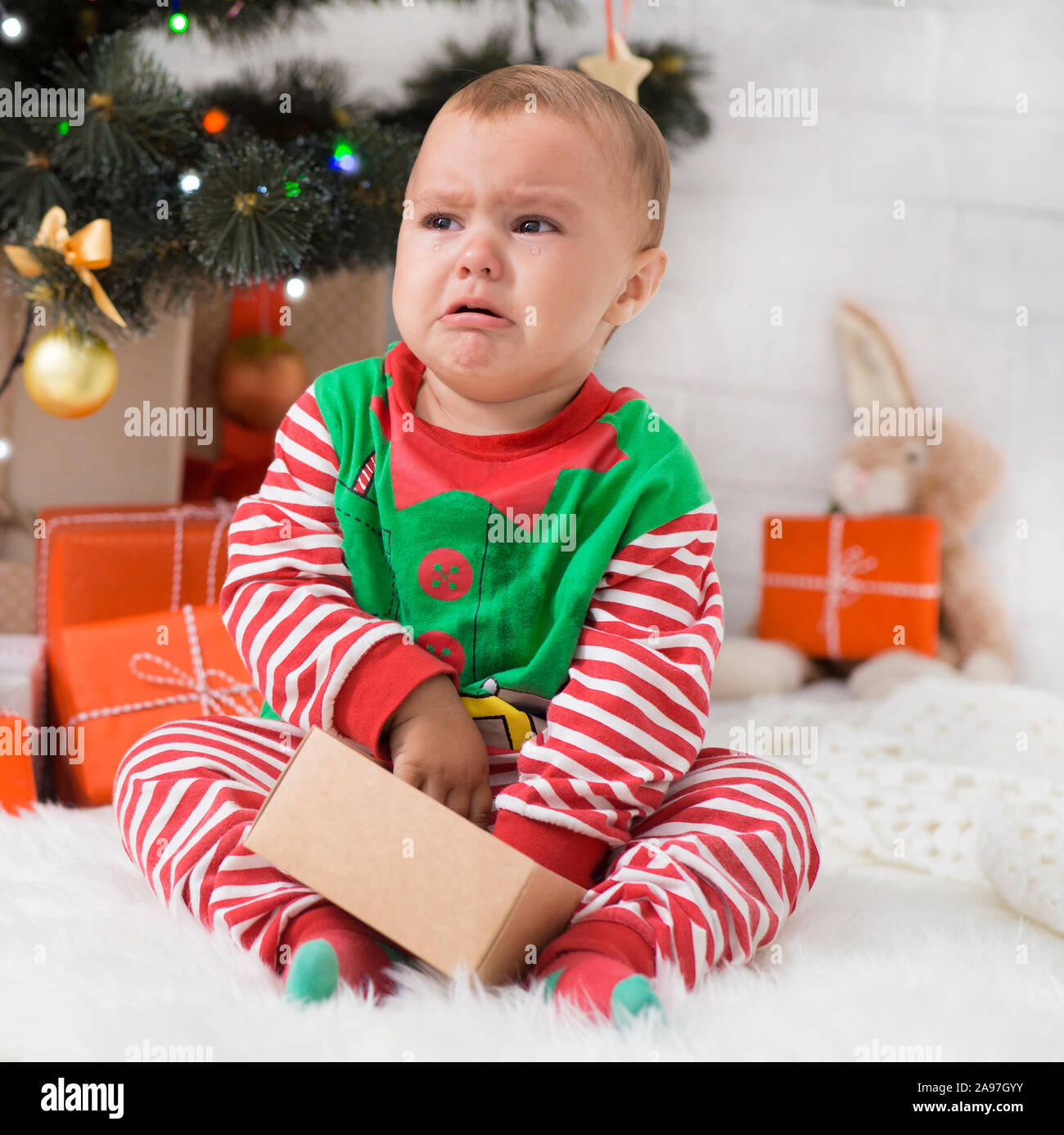 Bad Christmas. Little baby elf with present box crying near Xmas tree, waiting for gifts Stock Photo - Alamy