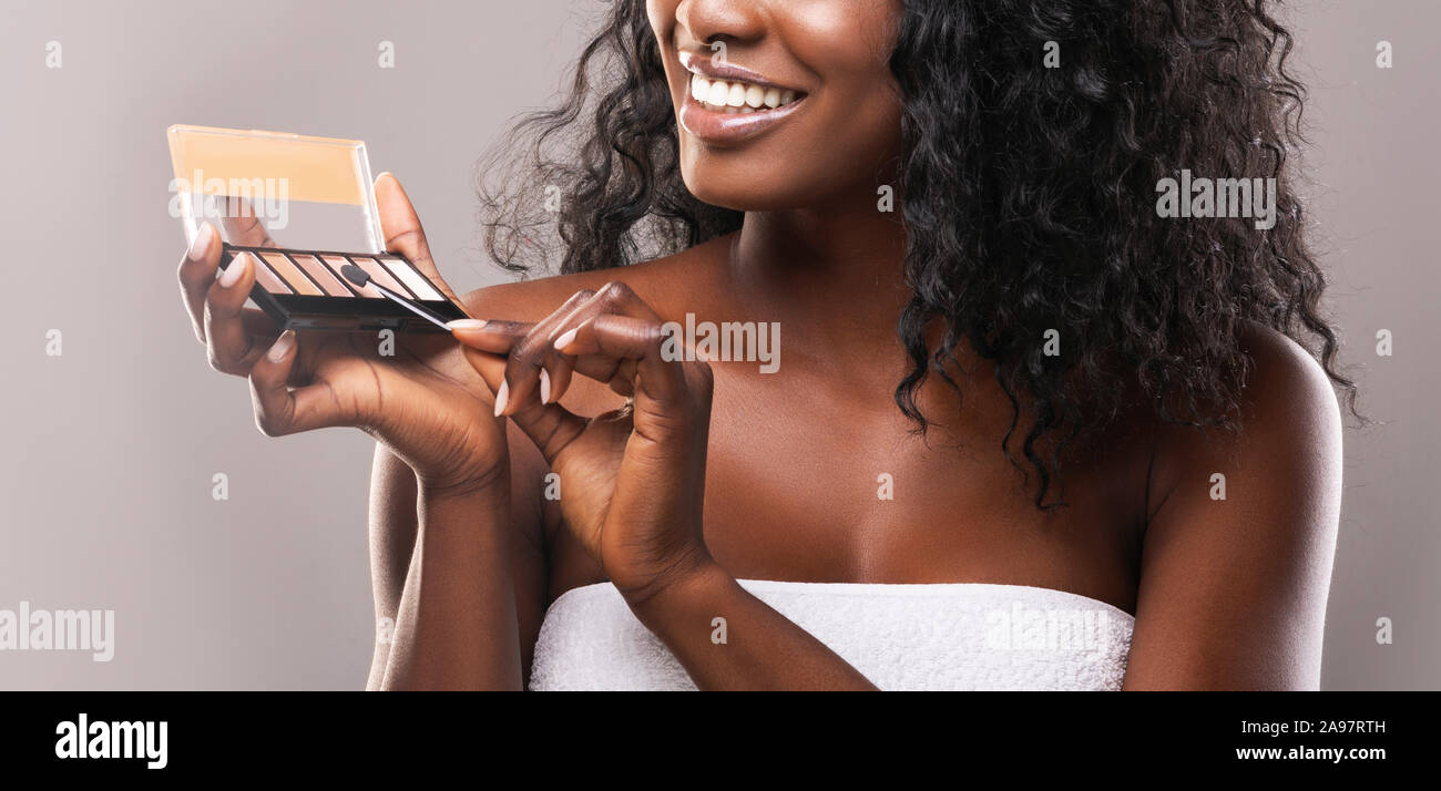 Makeup concept. Unrecognizable african american woman holding and testing eyeshadow palette, grey studio background, panorama Stock Photo