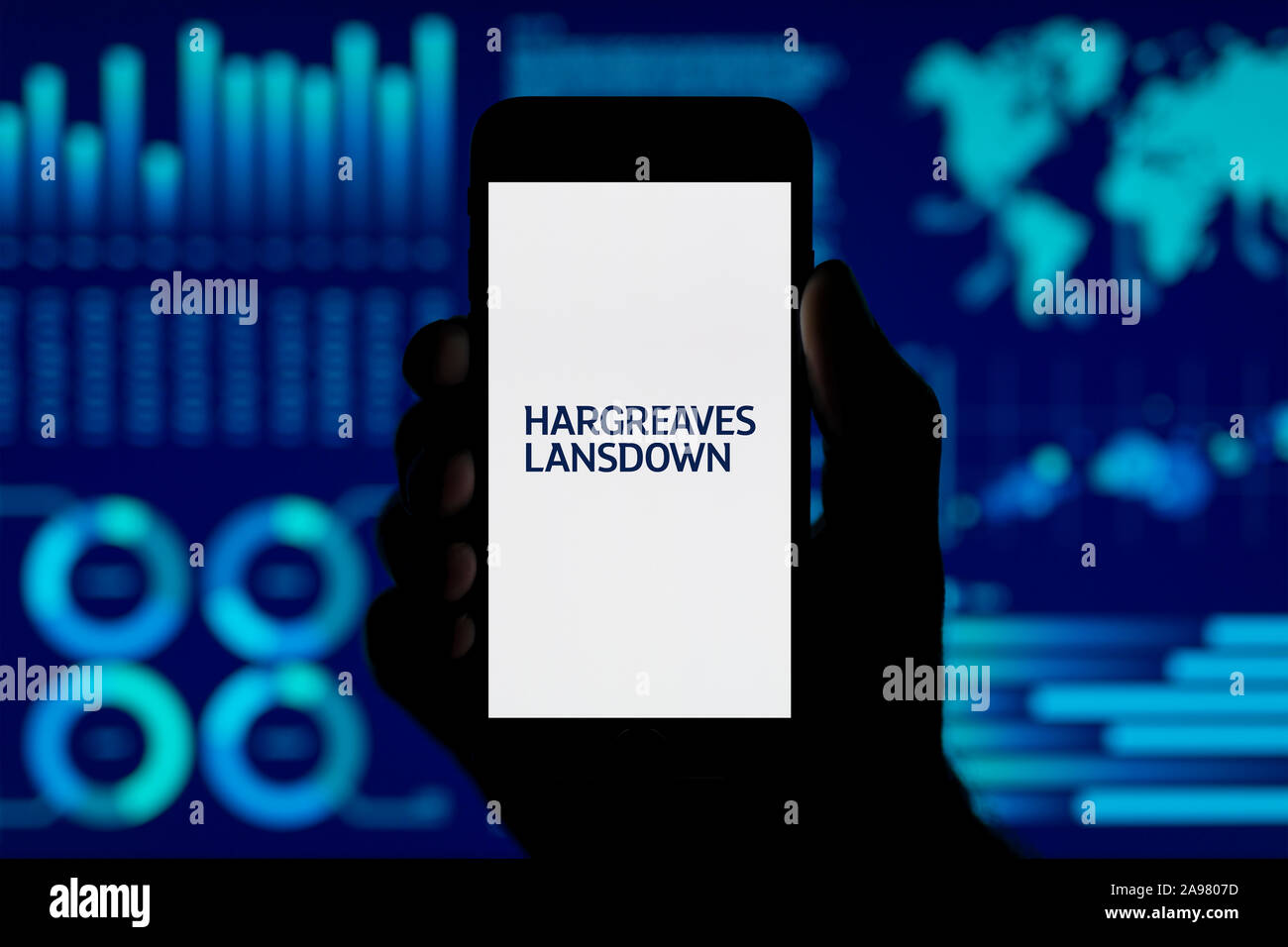 A man holds up an iPhone which displays the Hargreaves Lansdown logo, shot against a data visualisation style background (Editorial use only). Stock Photo