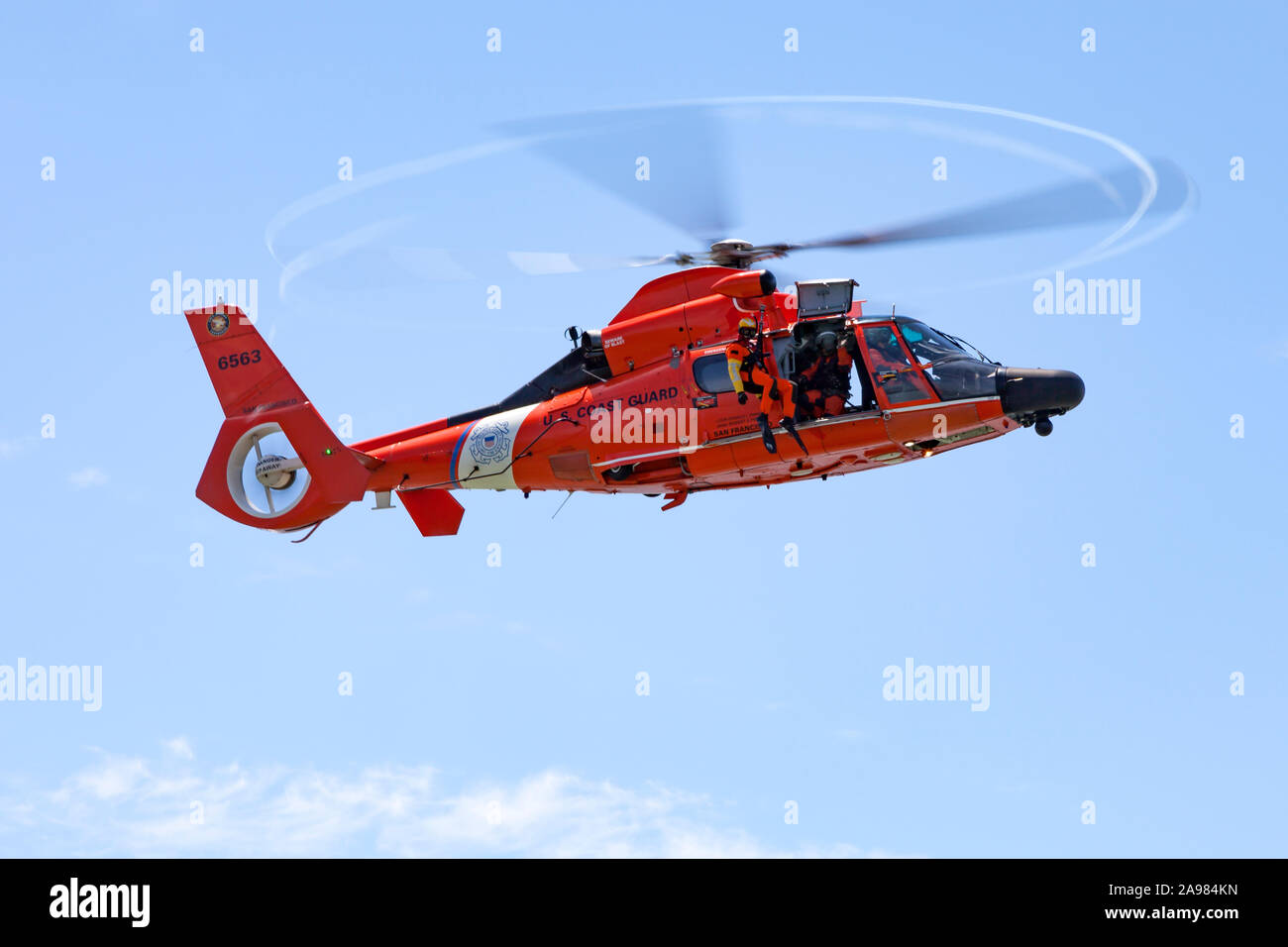 A USCG swimmer hangs from the hoist of an MH-65 Dolphin helicopter Stock Photo