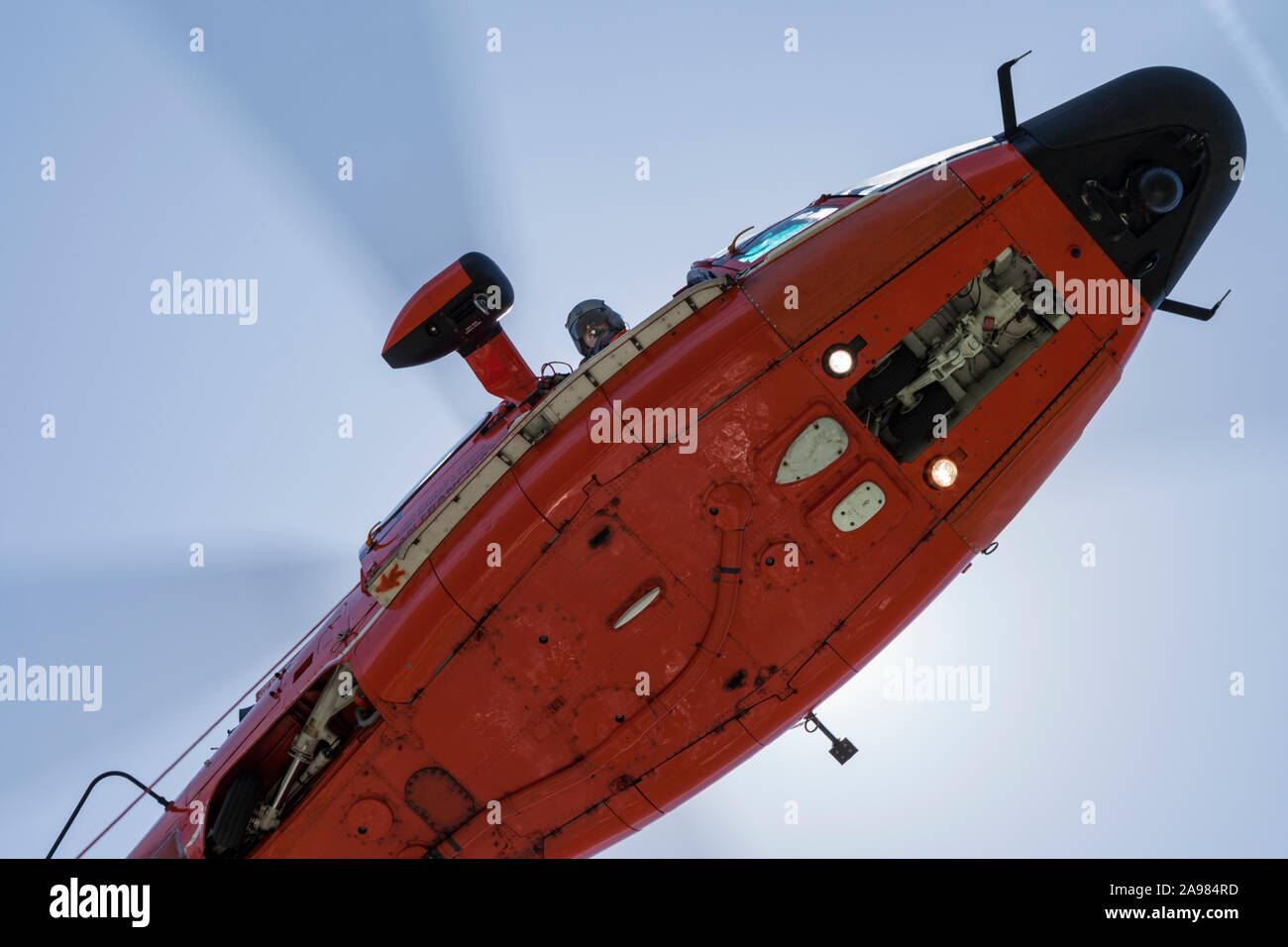 Flight Engineer looks down from the door of an USCG MH-65 Dolphin helicopter as he lowers a trail line. Stock Photo