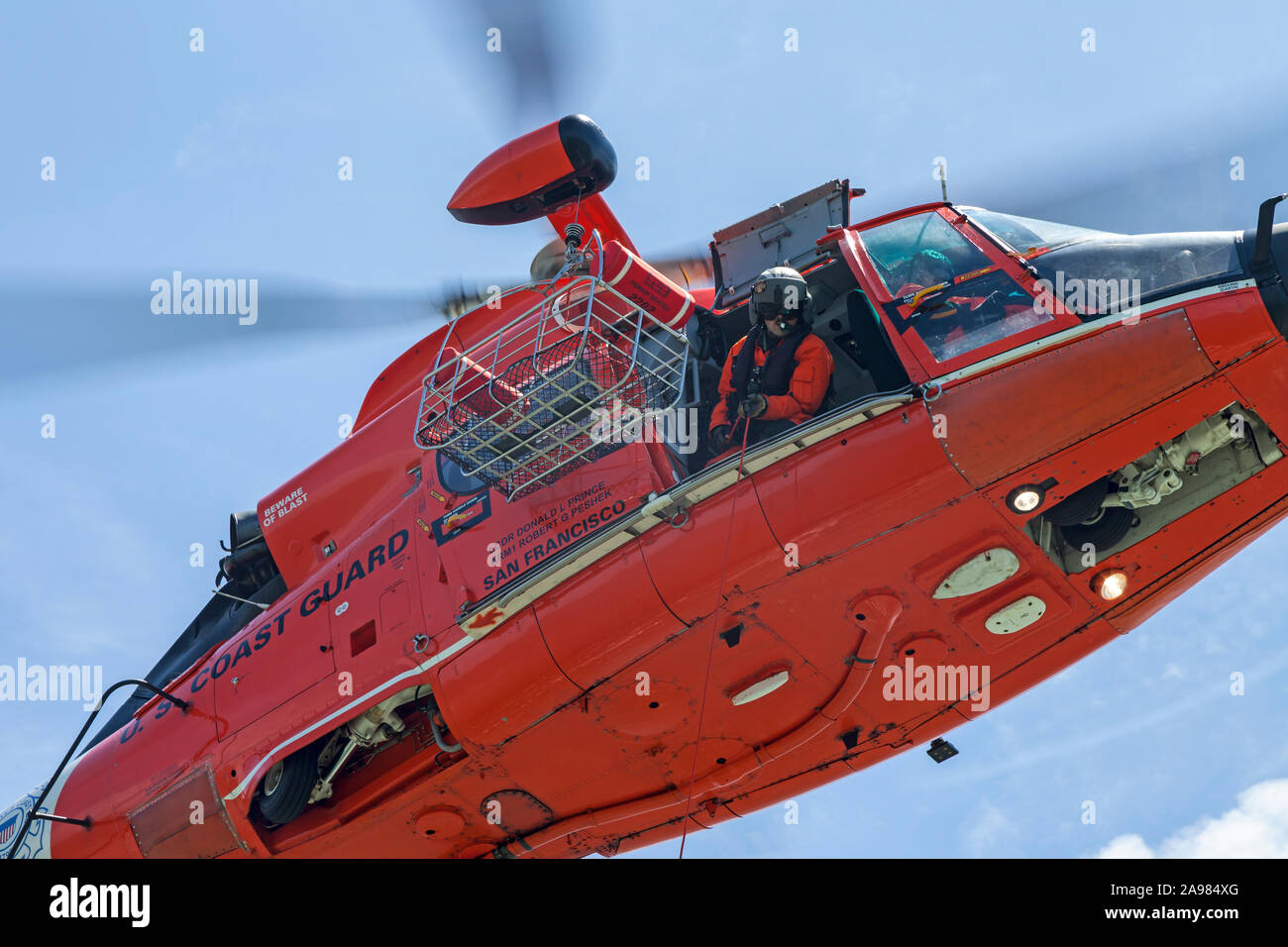The Flight Mechanic lowers a trail line from a USCG MH-65 Dolphin helicopter. Stock Photo