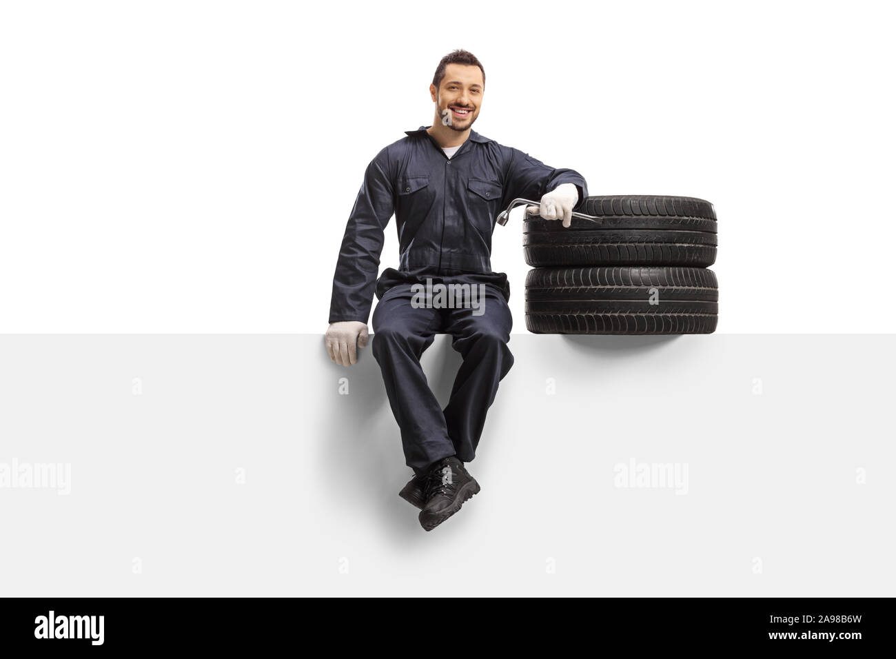 Auto mechanic sitting on a panel with tires and a wrench isolated on white background Stock Photo