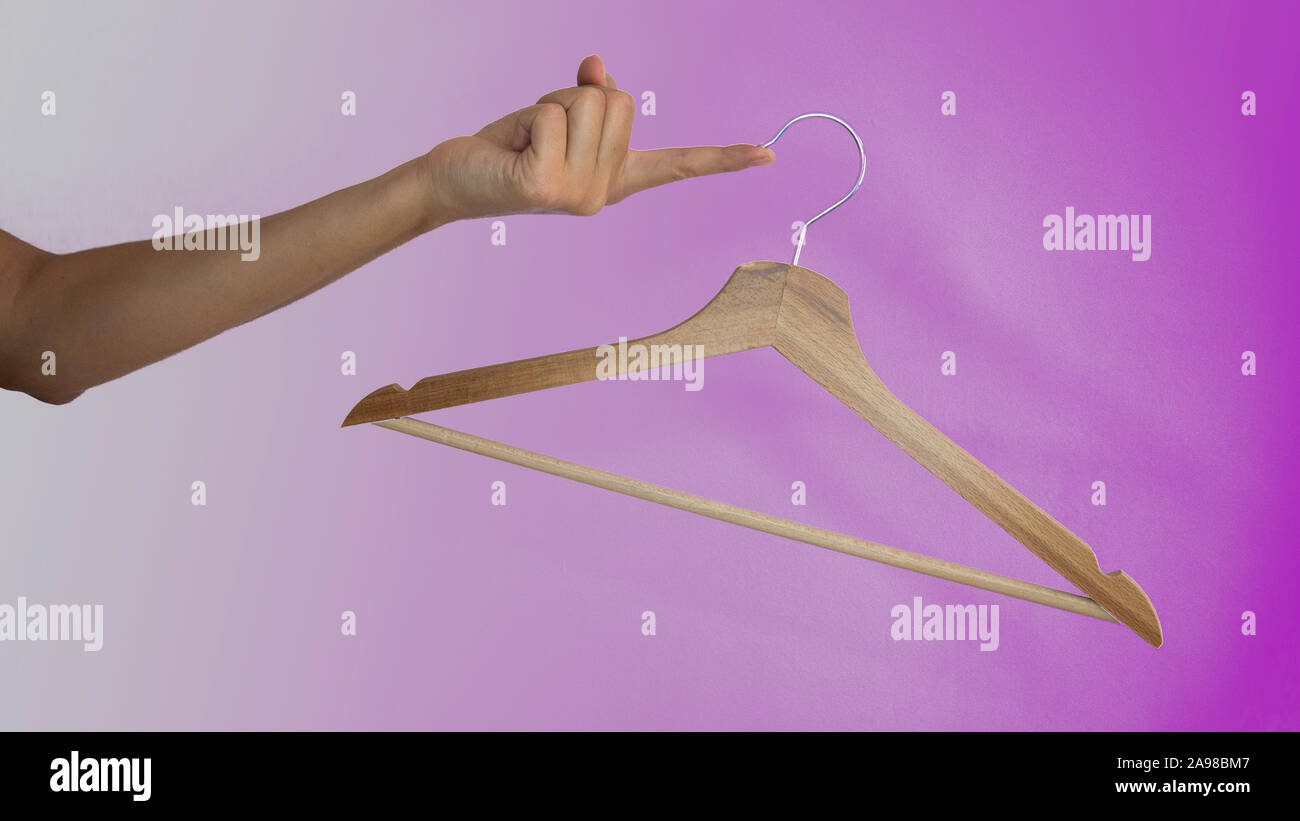 Wooden clothes hanger hanging from a female finger on a purple background. Stock Photo