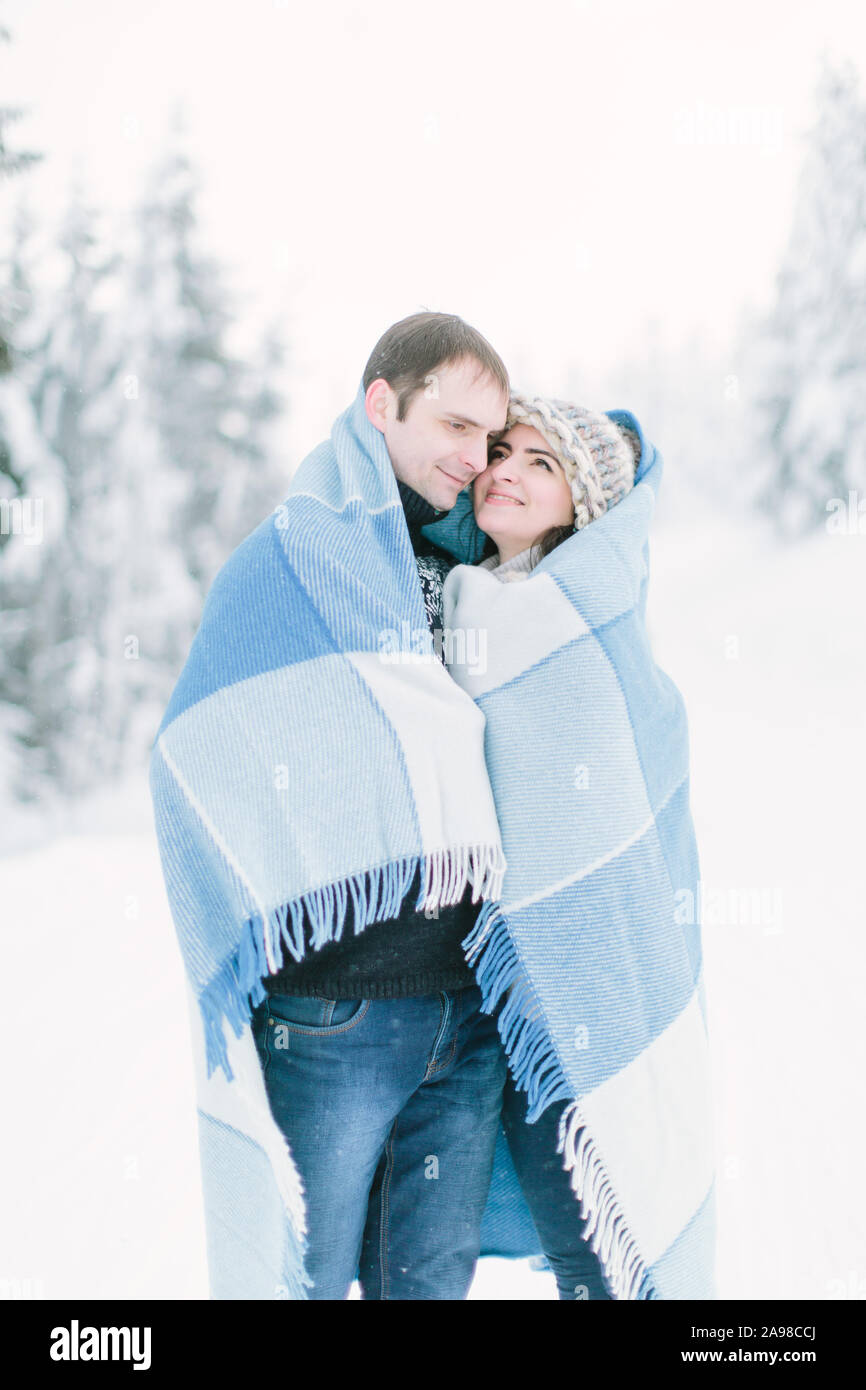 Happy lovely couple walking in winter frosty forest and covering with blue chekered wool blanket Stock Photo
