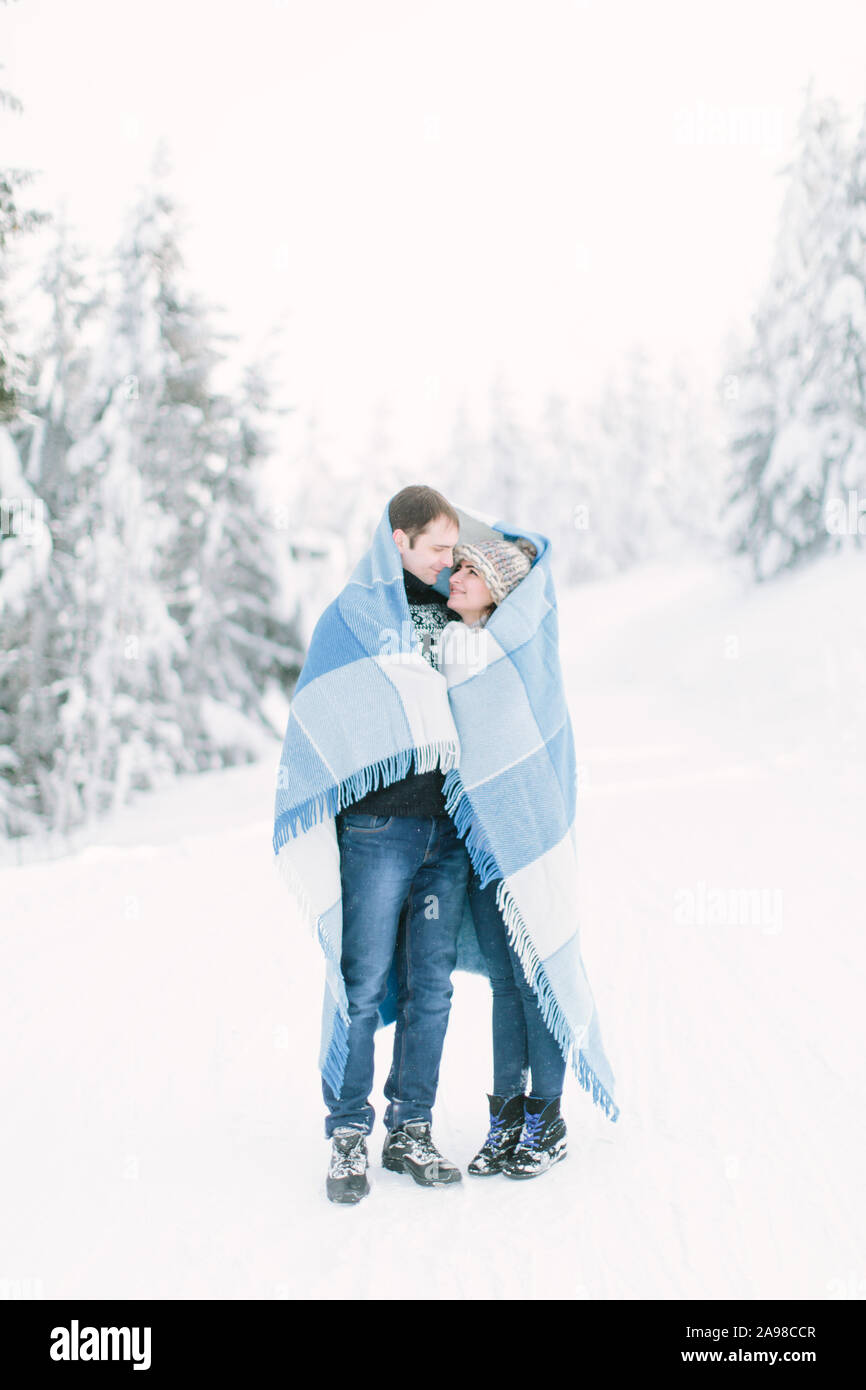 Happy lovely couple walking in winter frosty forest and covering with blue chekered wool blanket Stock Photo