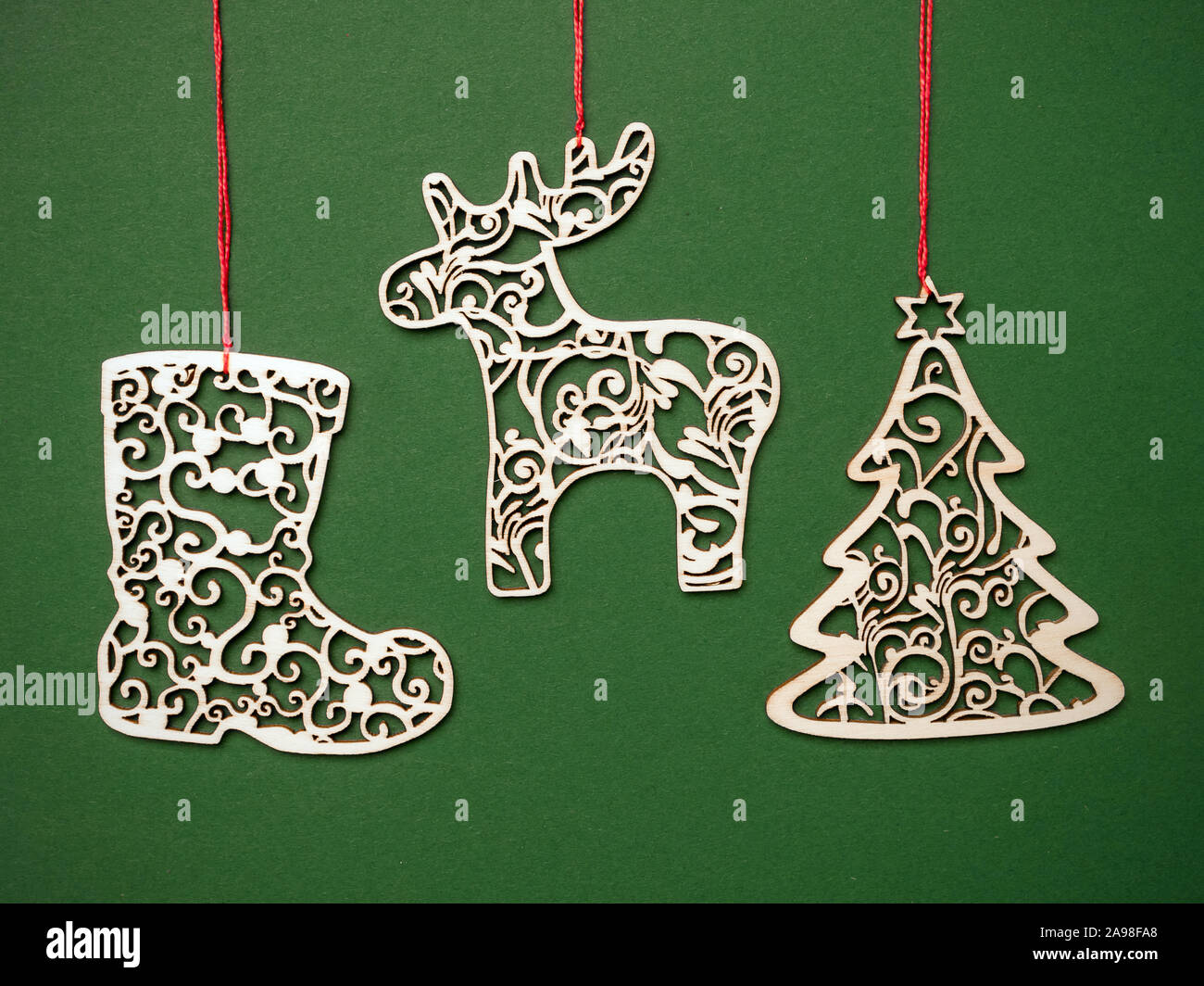 Christmas wooden ornamental cut-out decorations hung on red string against green background Stock Photo