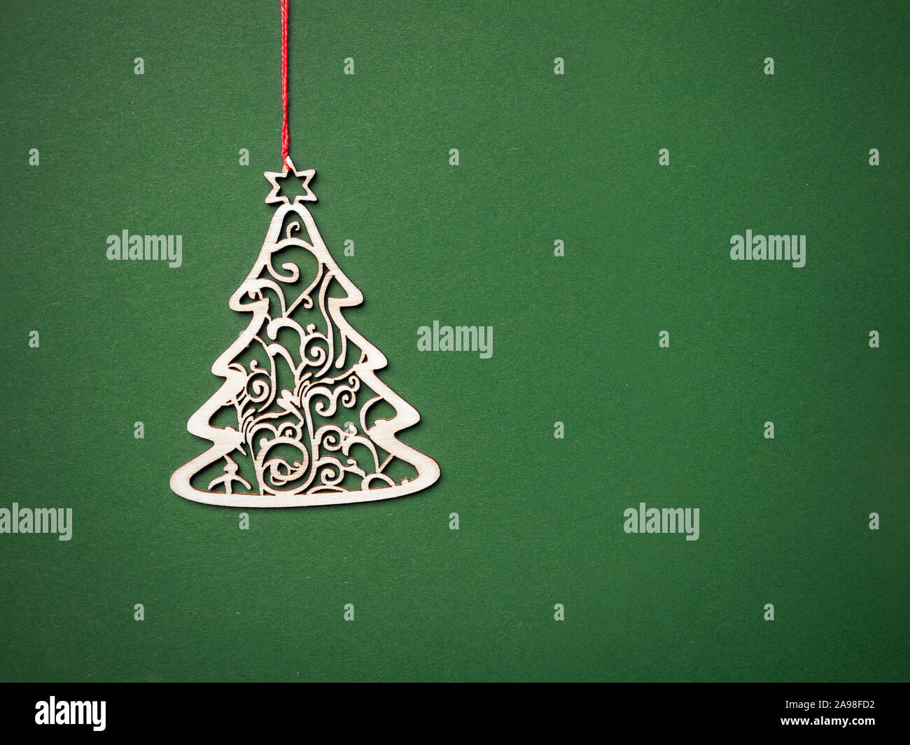 Wooden cut-out ornamental christmas tree hanging on red string against green background Stock Photo