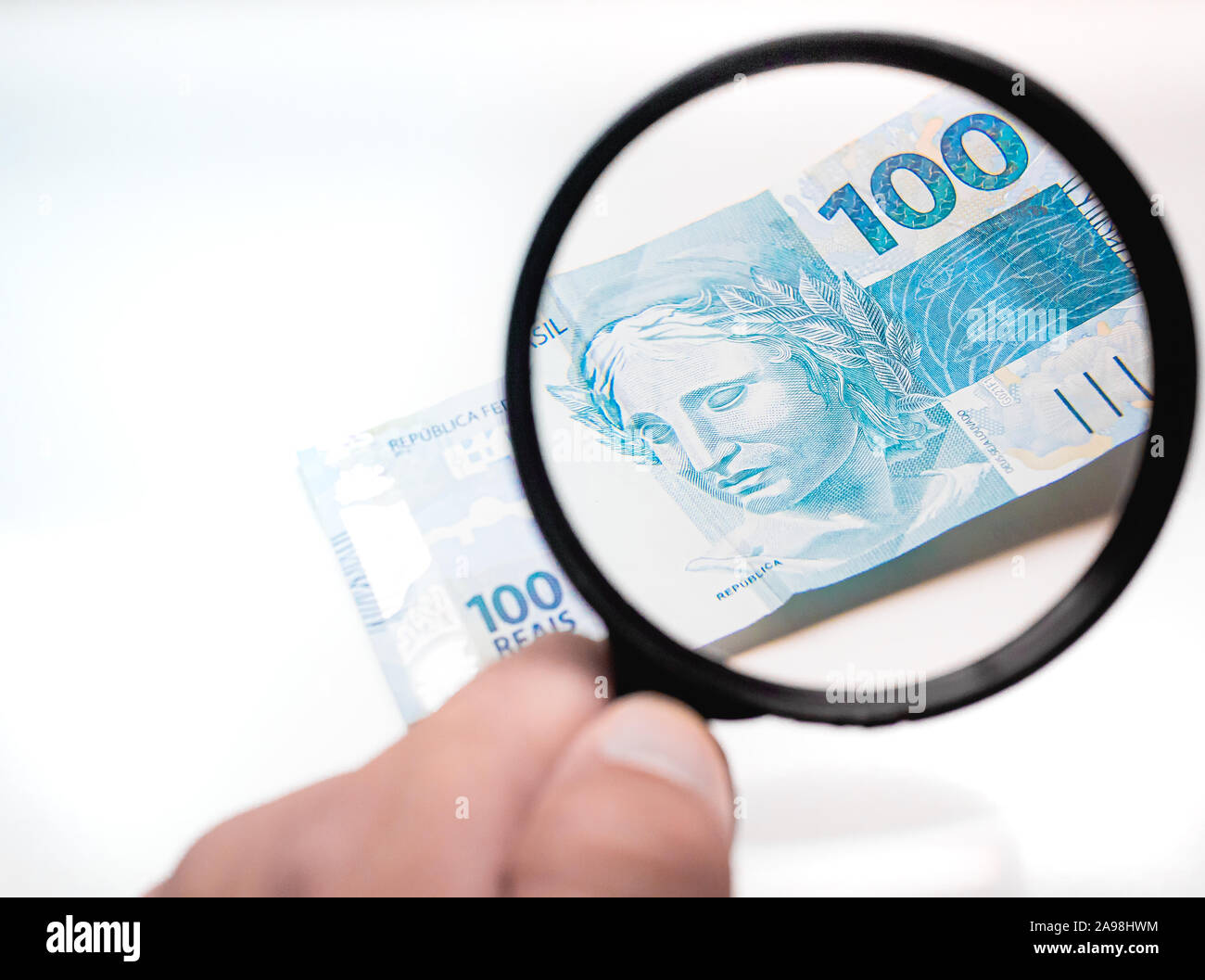 Real - Brazilian Currency. A hundred bill being seen by a man with a magnifying glass. Stock Photo