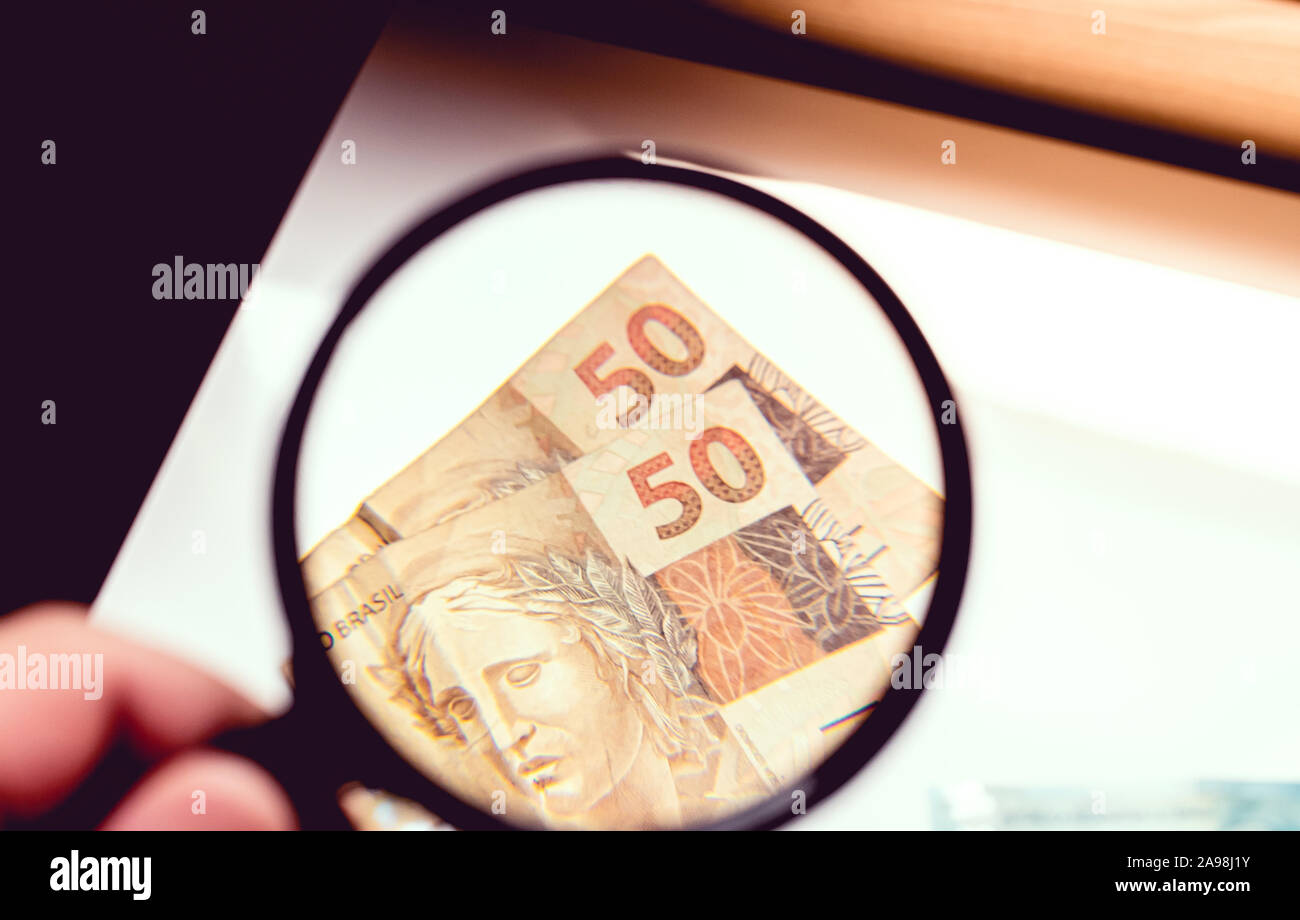 Shot of a man holding a magnifying glass visualizing fifty reais