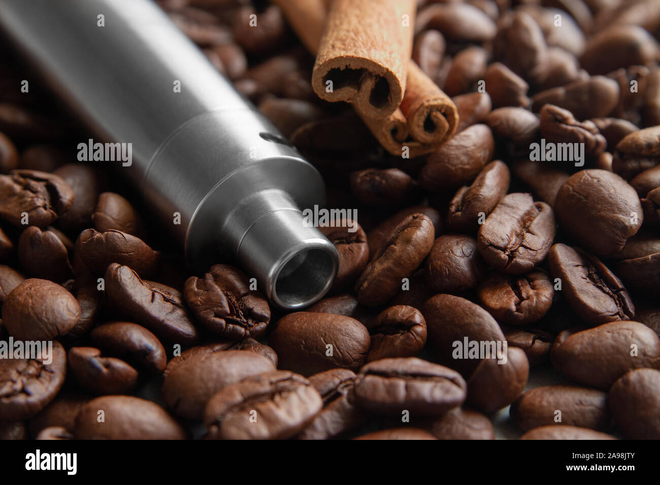 Concept of Coffee and canella E-Juice Flavor with copy space.  Vape Pen Kit and cinnamon lies on the background of Soft focused coffee beans. Stock Photo