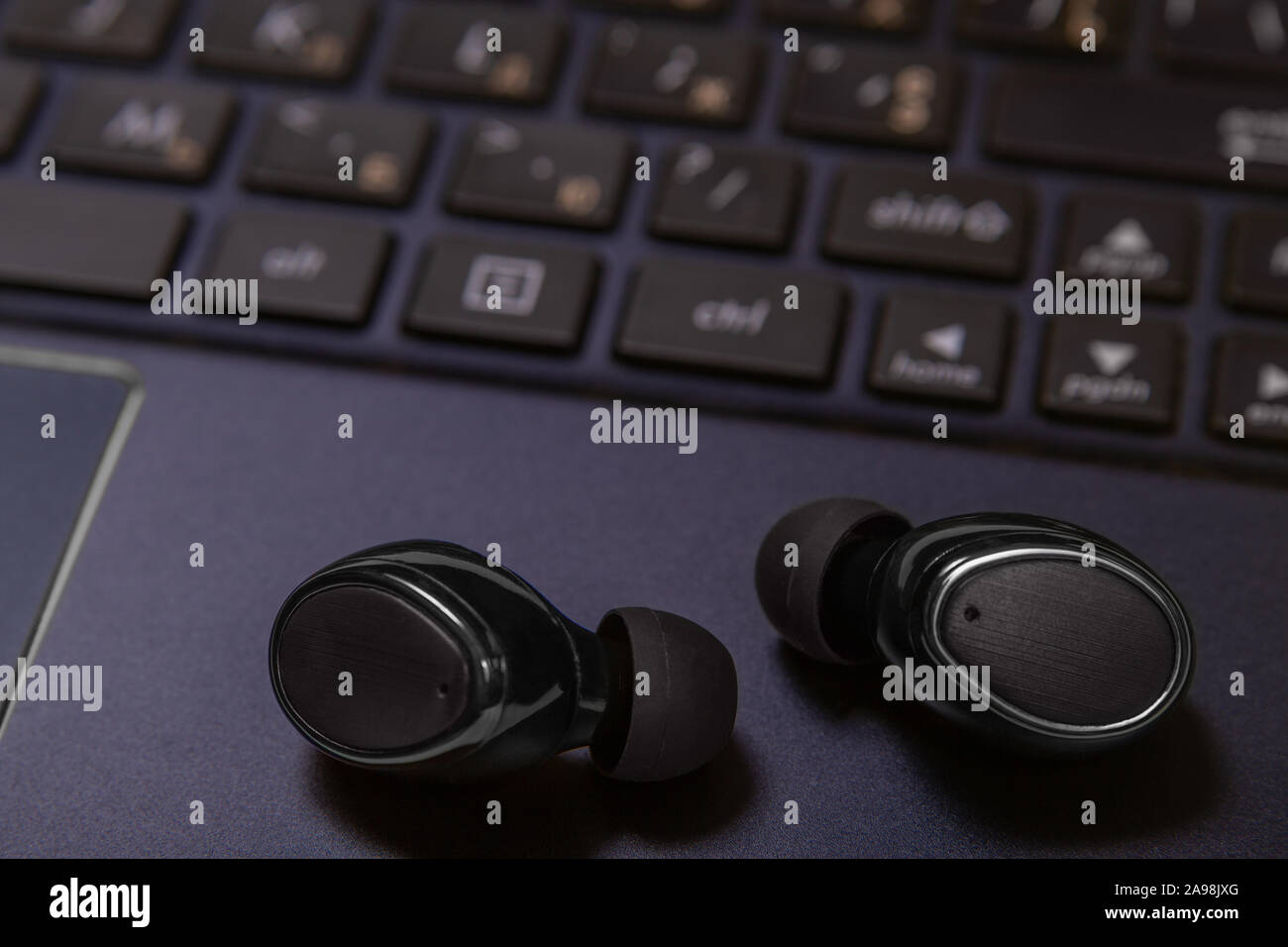 Close-up of wireless earpieces lying on a laptop keyboard Stock Photo