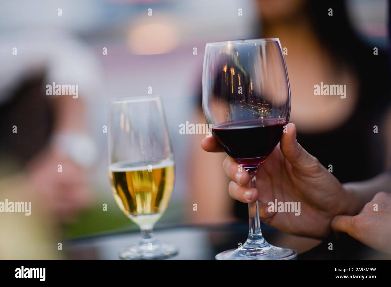 Hand holding a glass of red wine on a table next to a glass of beer. Stock Photo
