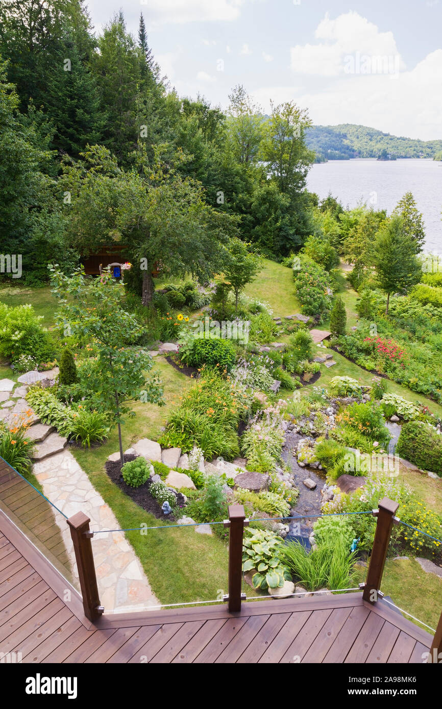 Top view of sloped residential backyard garden with rock edged stream bordered by orange Hemerocallis - Daylily, pink Astilbe flowers Stock Photo