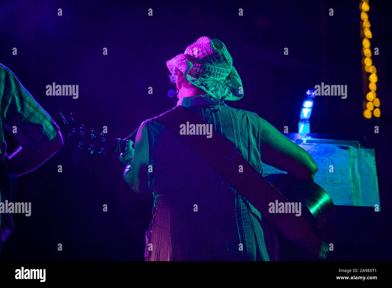 Backside view of adult female guitarist performing on stage playing her guitar with bokeh lights